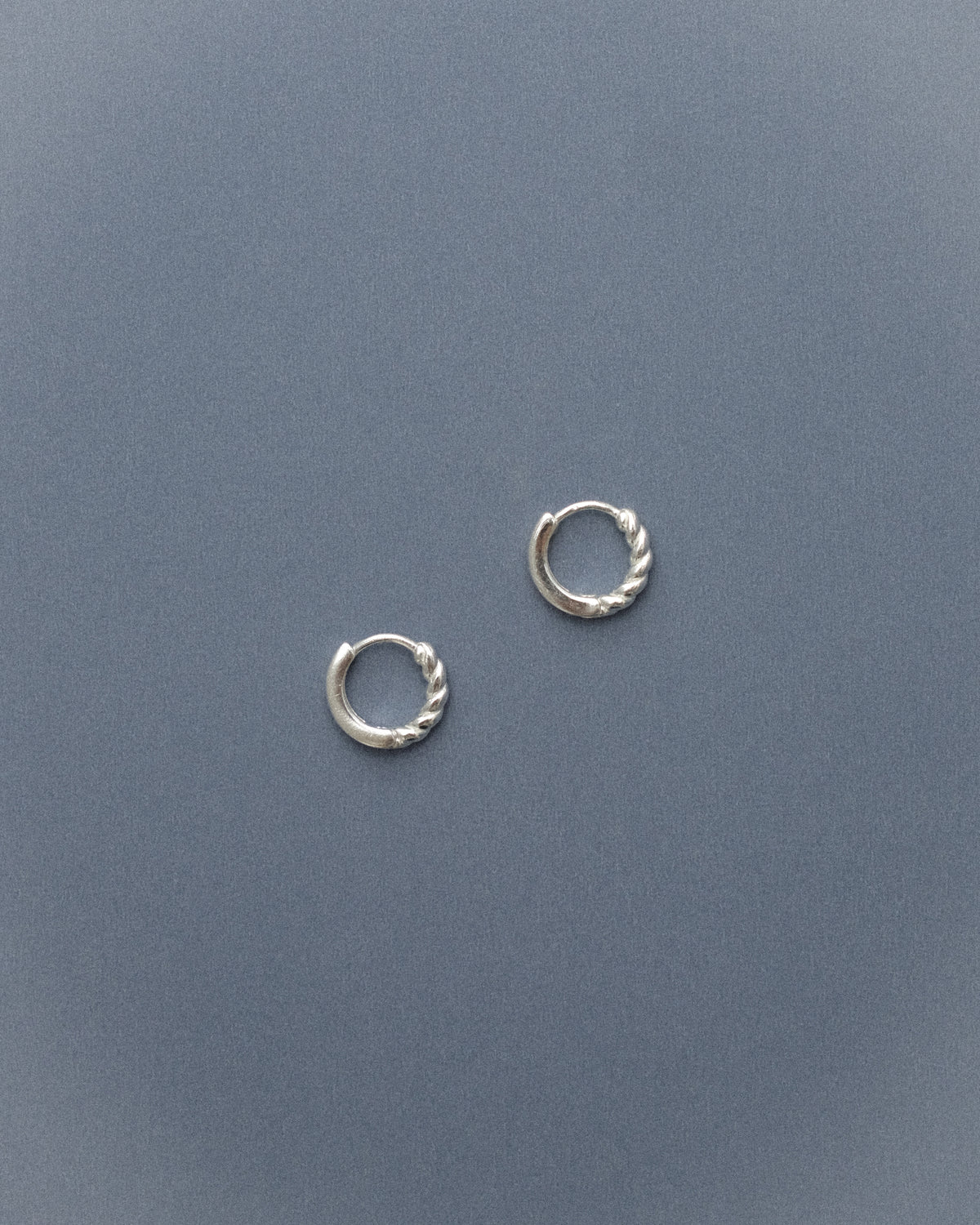 Pair of revisible silver hoop earrings on a grey-blue background