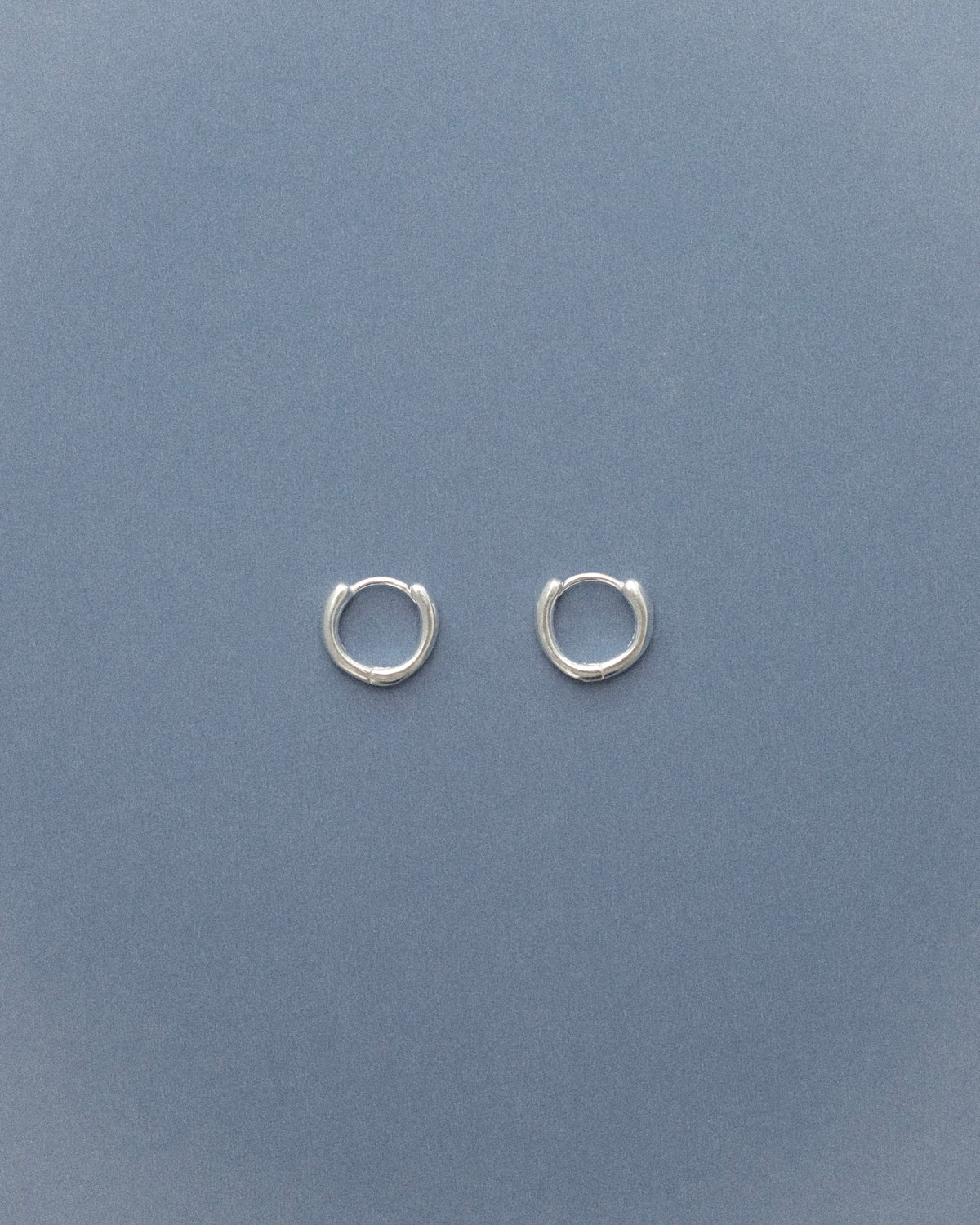 Small silver sulptural hoop earrings on a grey blue background