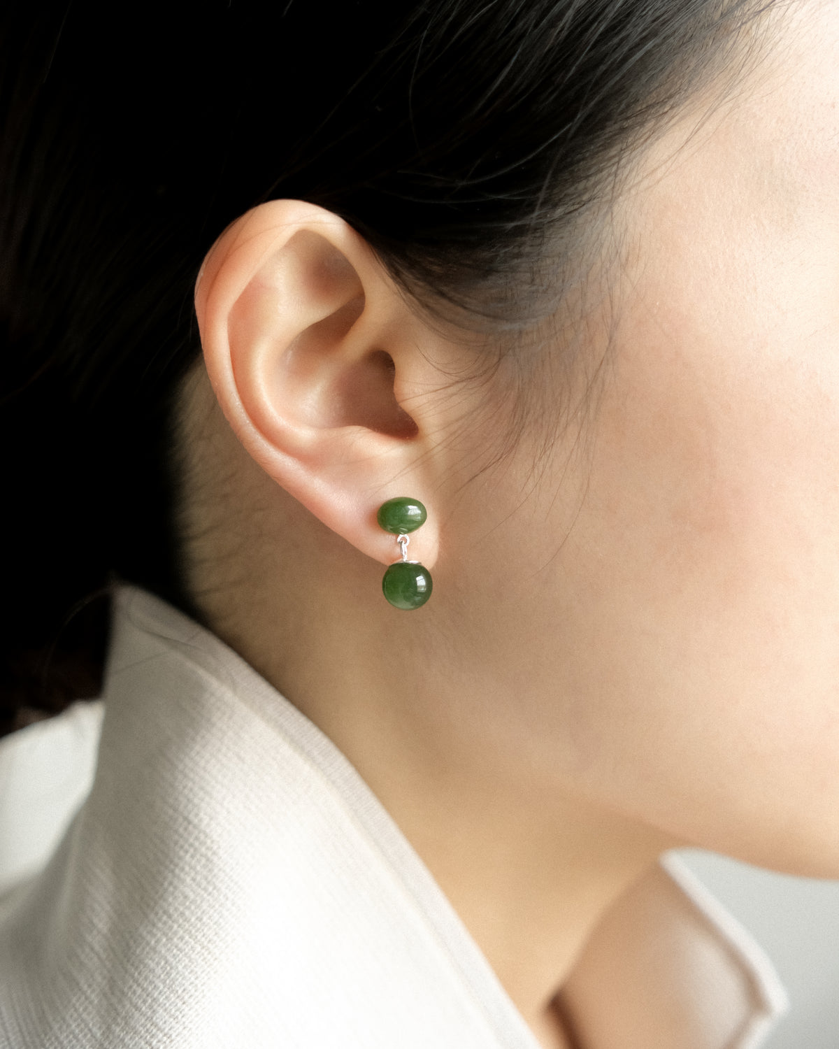 Close-up of an ear wearing a nephrite jade drop earring with a white background