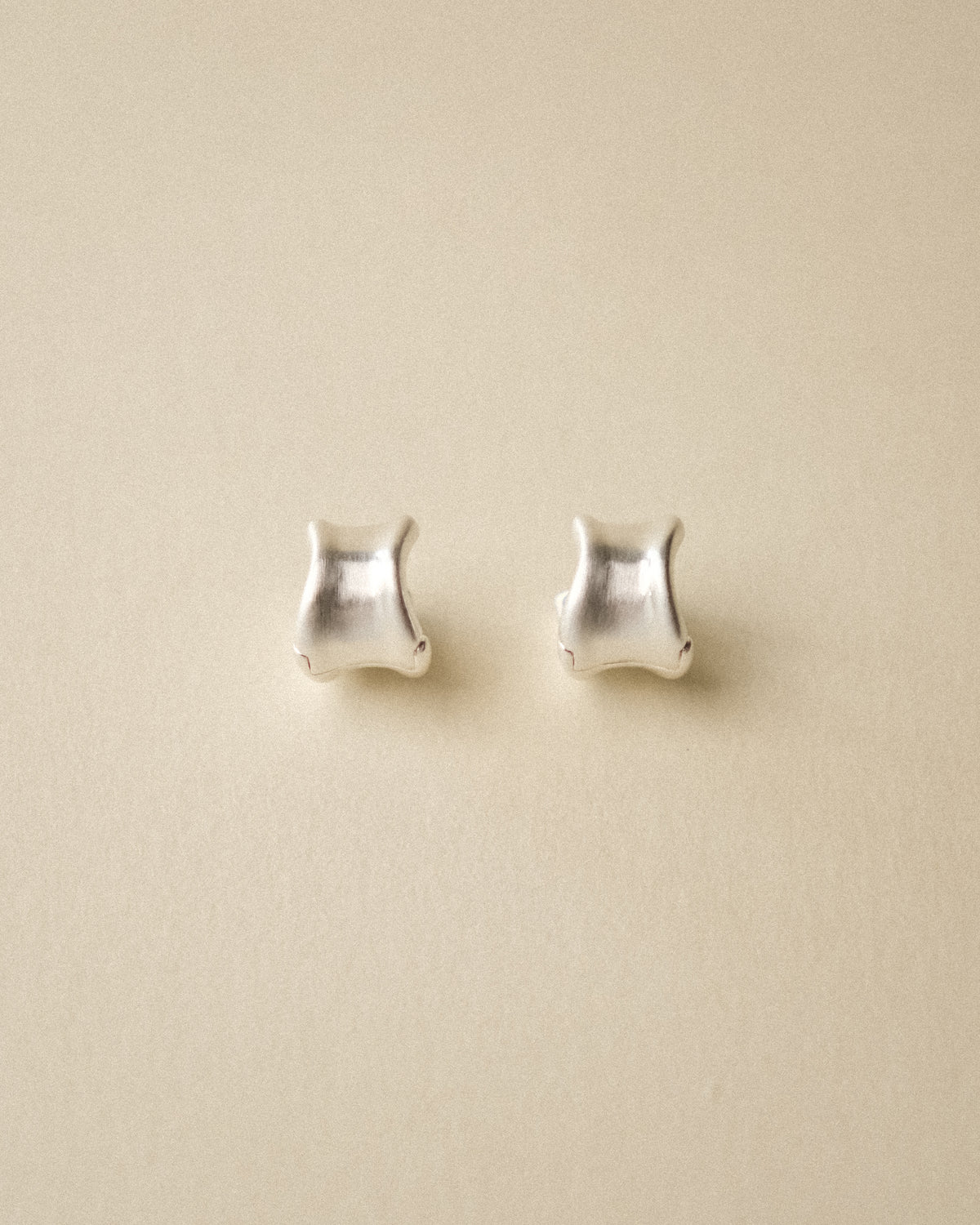 A pair of brushed curved earrings shoot against of a warm background.