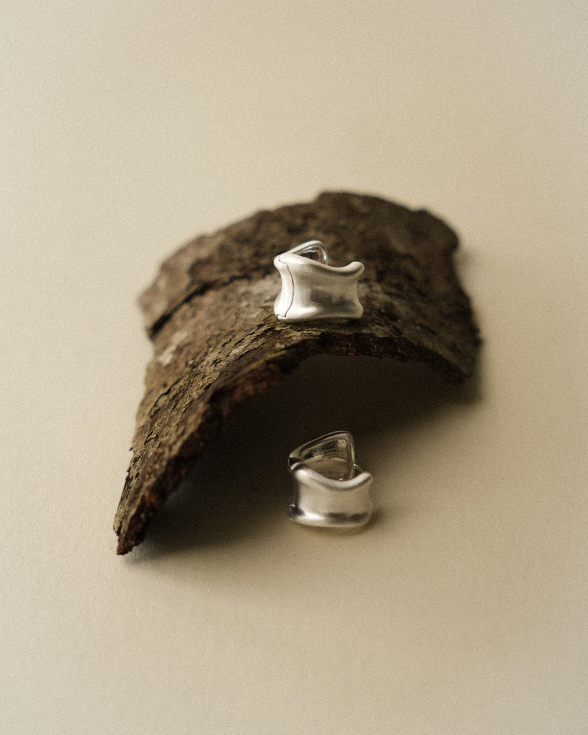 A pair of curved earrings shot with natural tree bark from the front, against a warm backdrop.