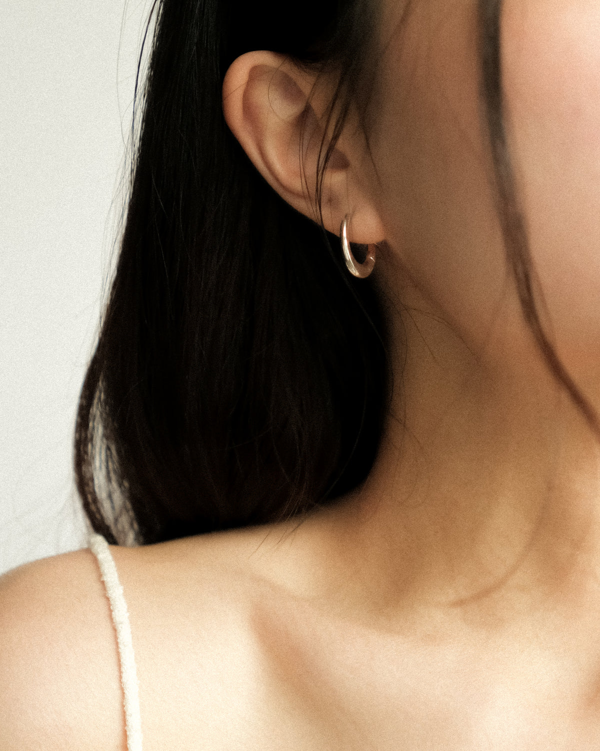 A close up of a woman wearing pebble shaped hoop earrings, photographed from the front with her hair falling elegantly against a clean white background.
