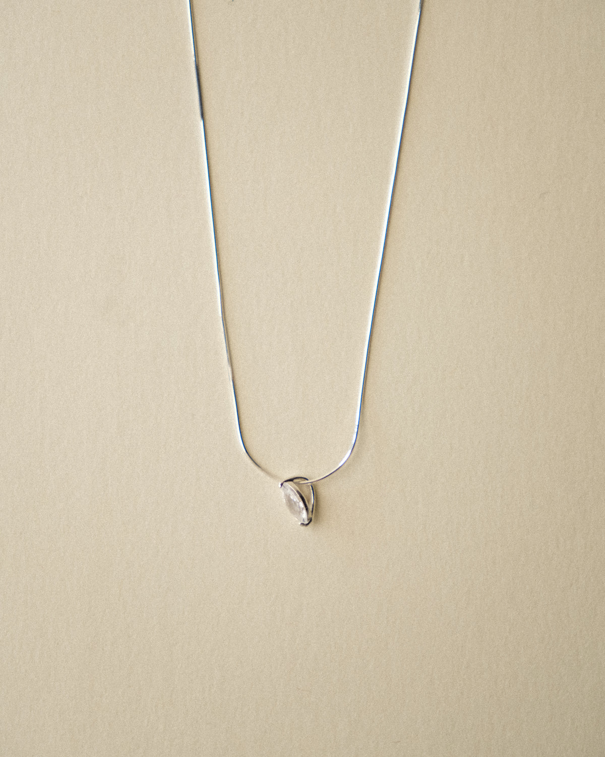 A close-up of a marquise diamond pendant necklace captured from the side, unveiling its vase-inspired silhouette against a warm-toned wabi-sabi backdrop.