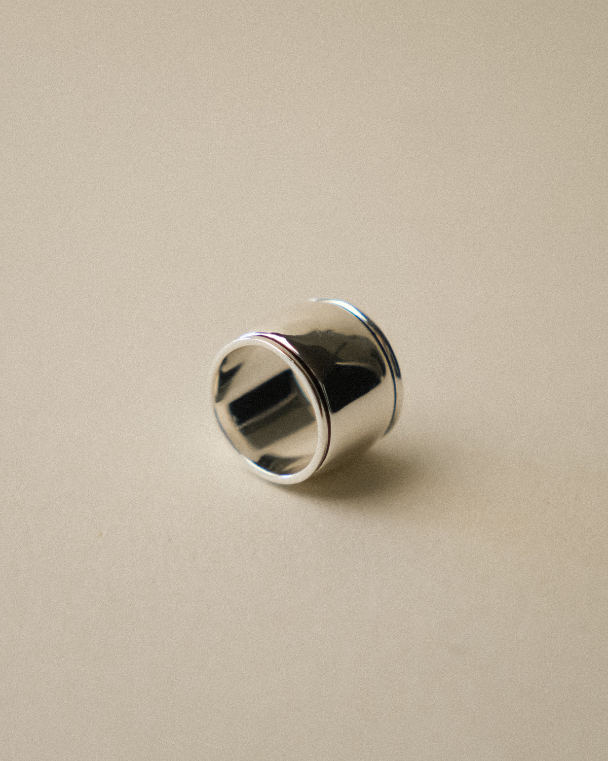 A front-facing shot of the bold sculptural cigar band ring against a warm-toned wabi-sabi backdrop.