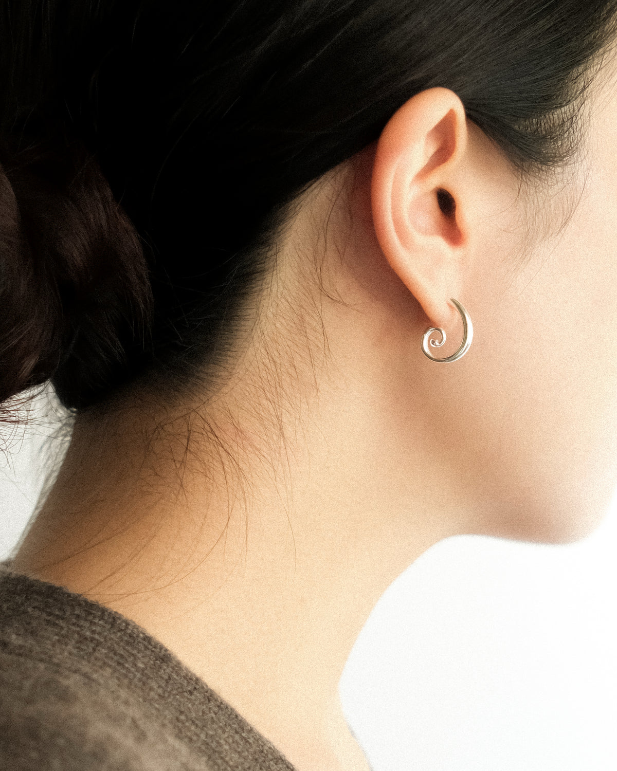 A close-up side-back profile of a woman wearing Art Deco spiral stud earrings, revealing the sculptural spiral silhouette and graceful curves against a clean white backdrop.