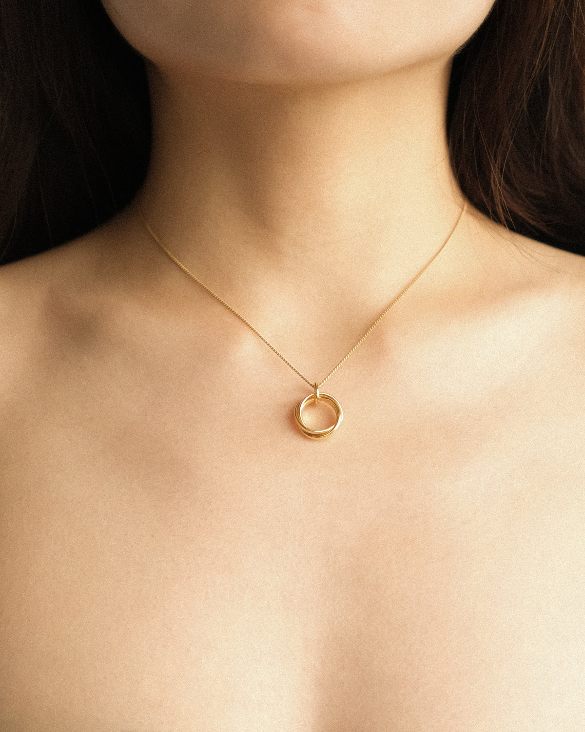 A close up of a woman adorned with the Trio Interlink pendant necklace in gold, capturing its quiet and timeless elegance.