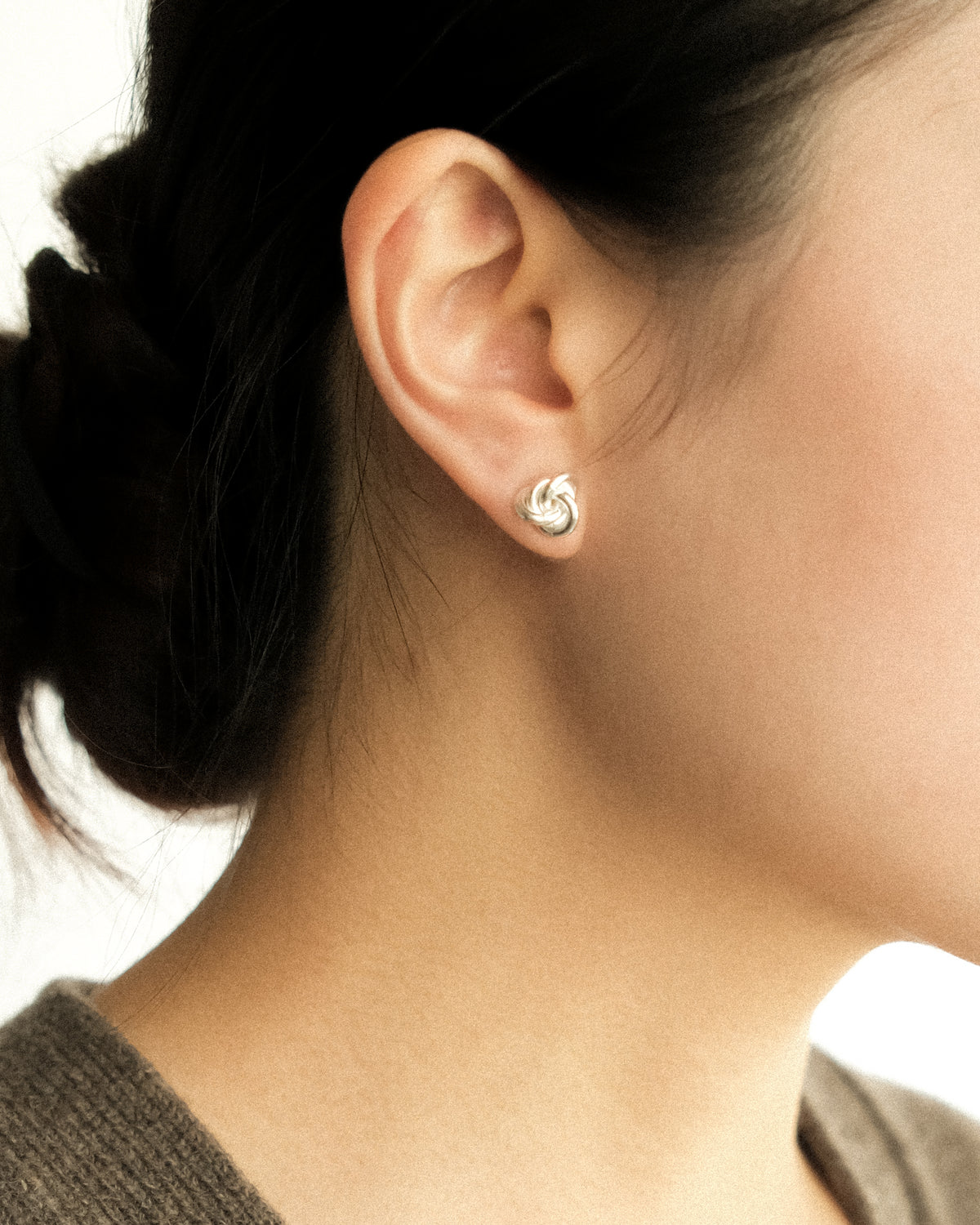A close-up of a woman's ear wearing a small silver knot stud earring.