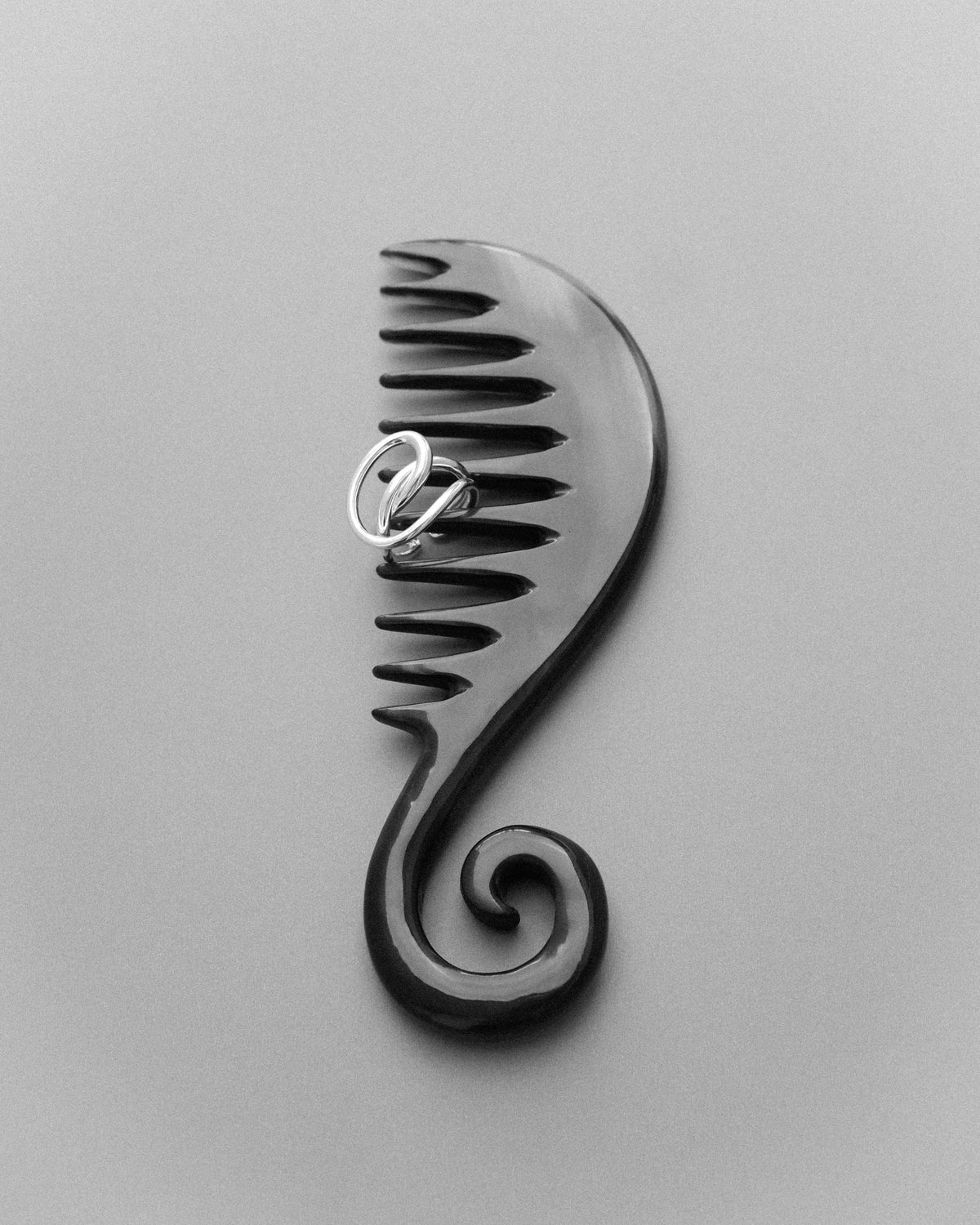 A black spiral natural horn comb displayed on a gray background, paired with a sculptural ring.