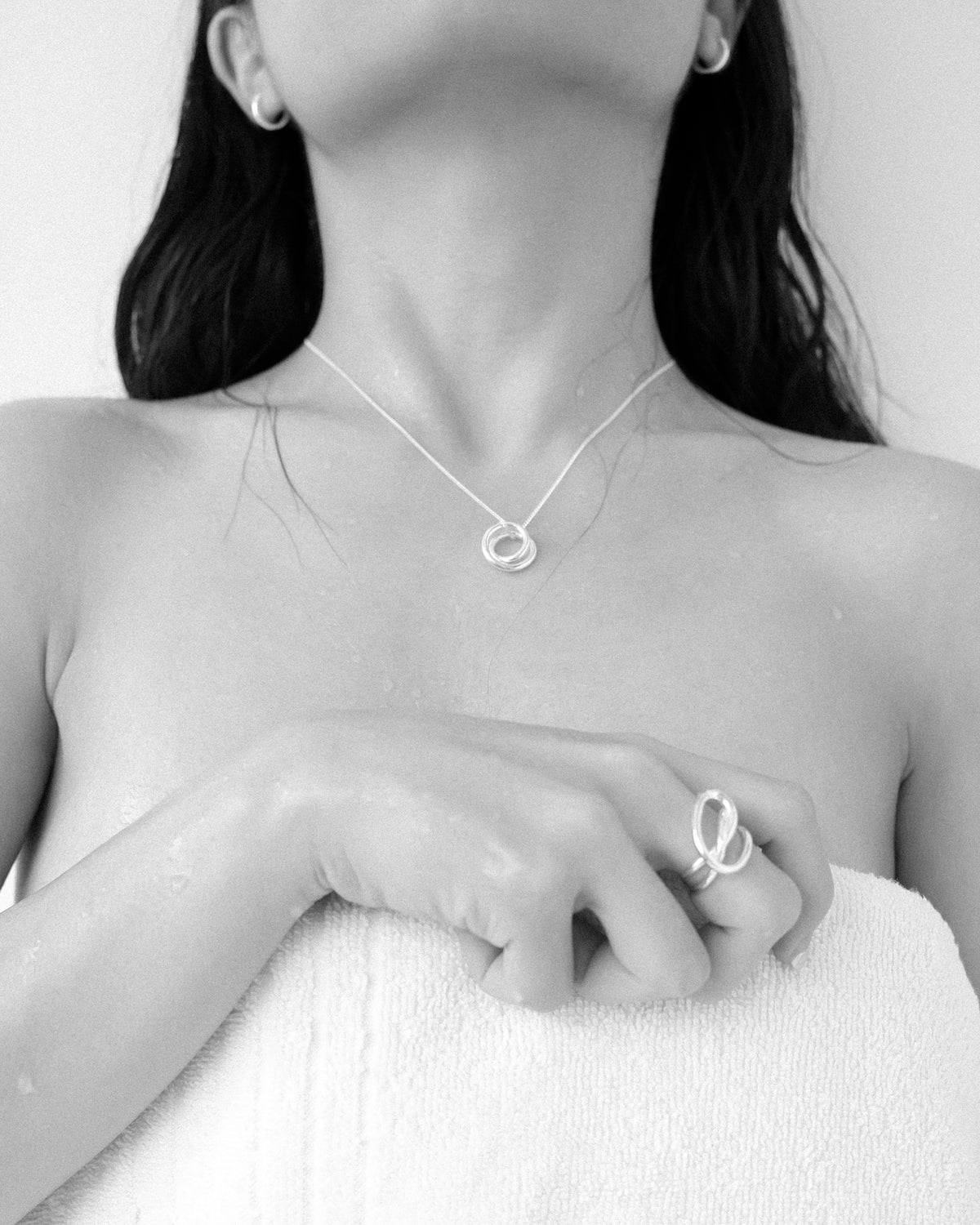 A woman adorned with a silver sculptural necklace, paired with minimalist hoop earrings and a matching ring, set against a clean, plain background. (black and white version)