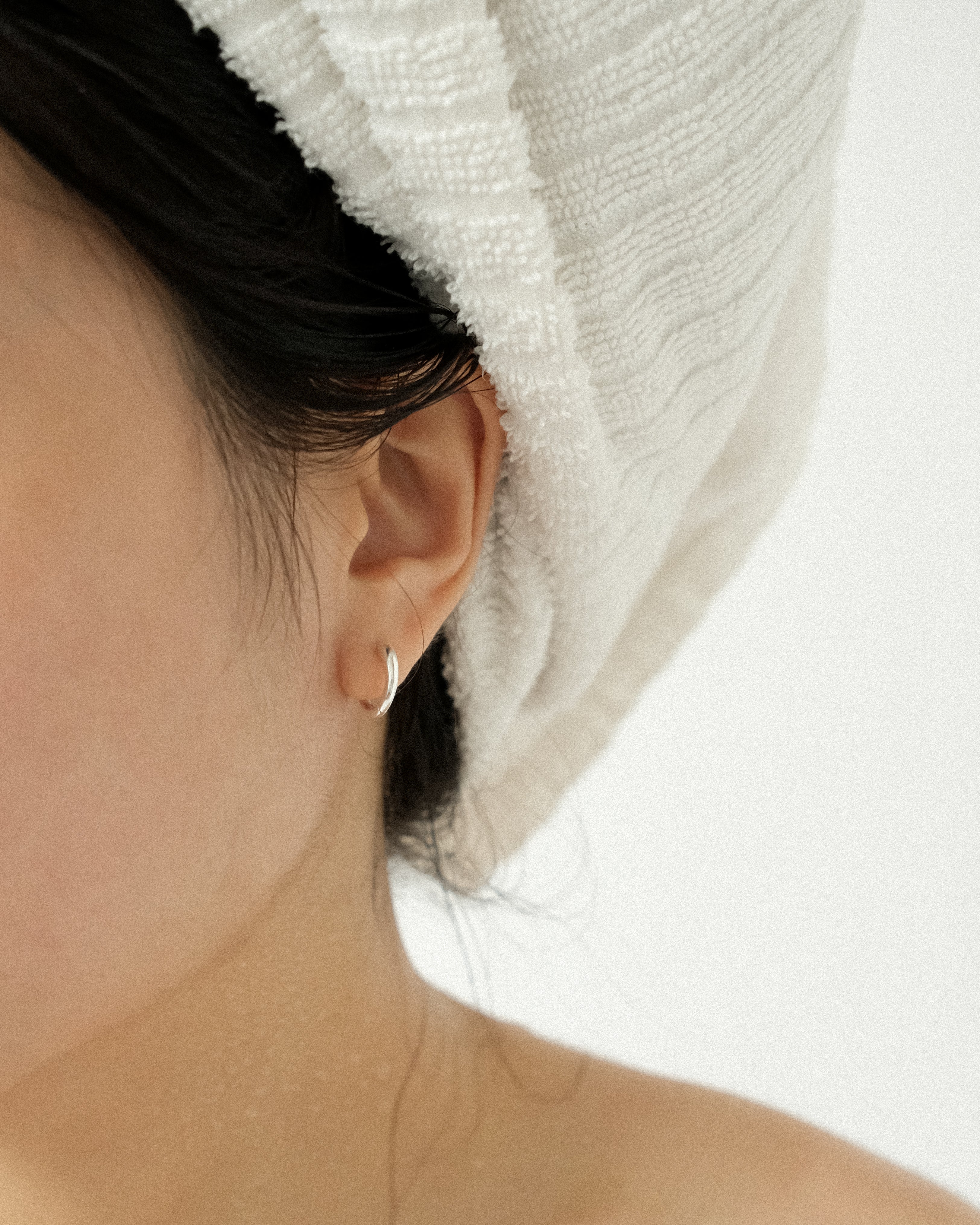 A close-up, an ear adorned with a silver hoop, hair wrapped in a white towel.