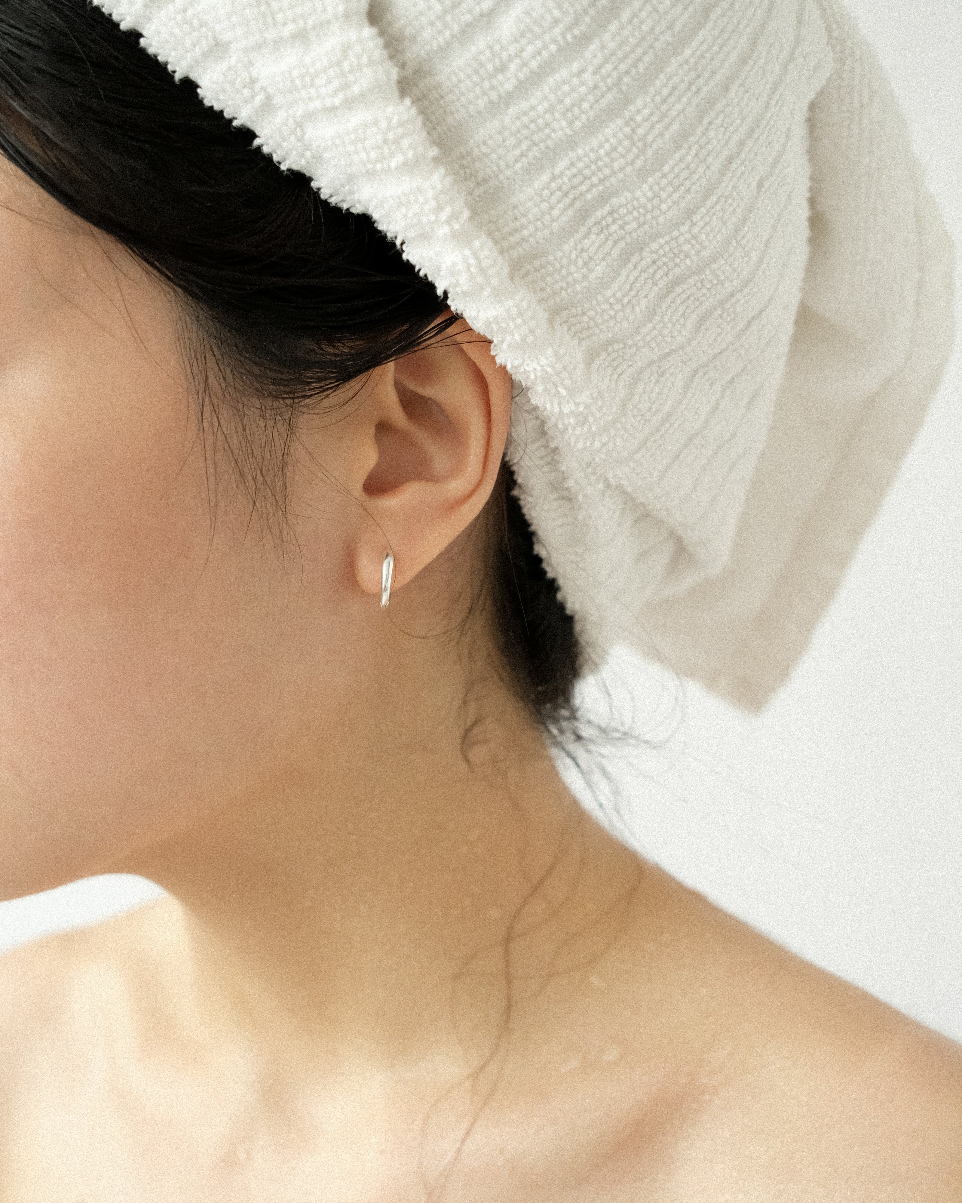Close-up of a person wearing a white towel on their head with a focus on an hoop earring.