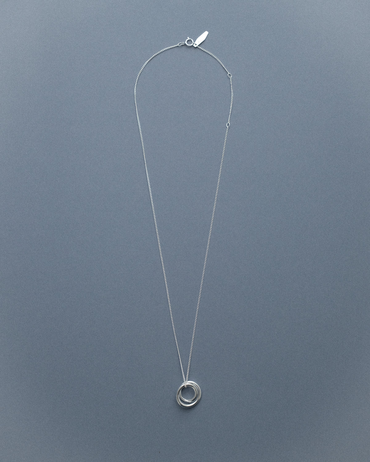 A silver line sculpture pendant necklace against a blue backdrop.