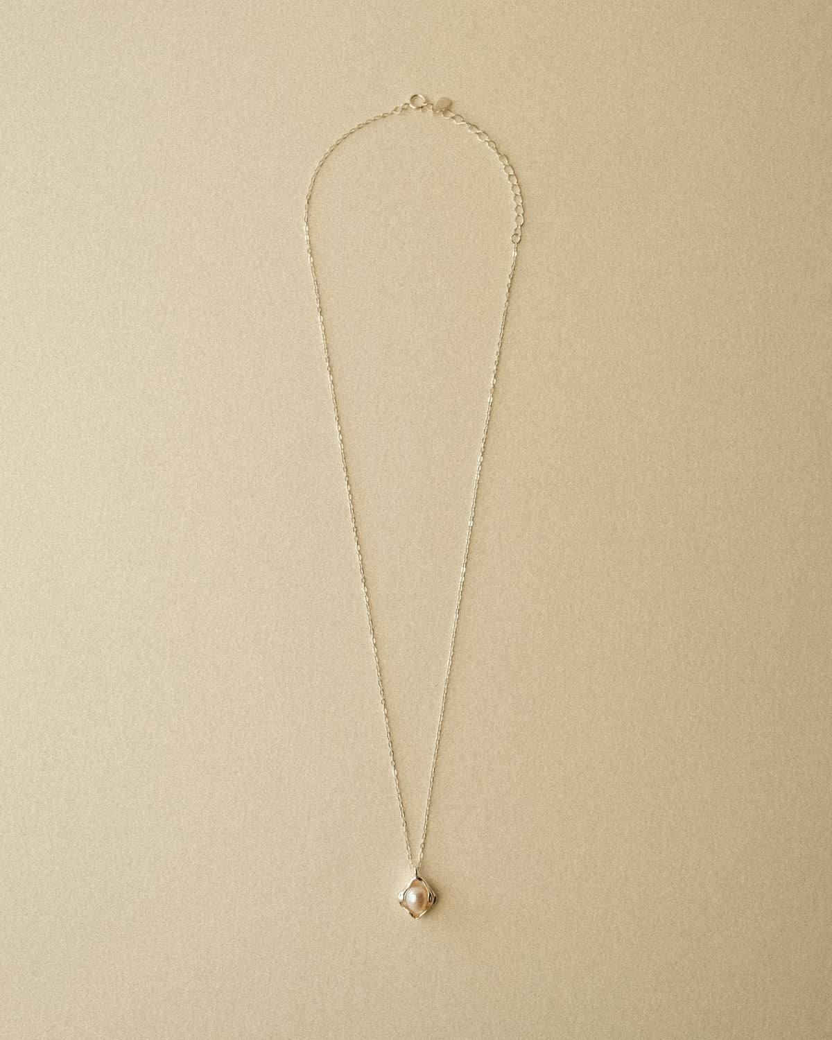 A delicate silver chain necklace with a small, petal-shaped pendant featuring a central freshwater pearl, displayed against a warm Wabi-Sabi-inspired background.