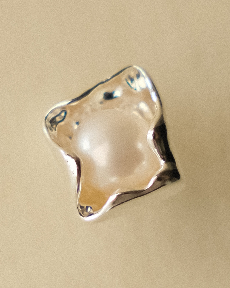 A close-up of a silver earring highlighting its geometric petal shape and central freshwater pearl.
