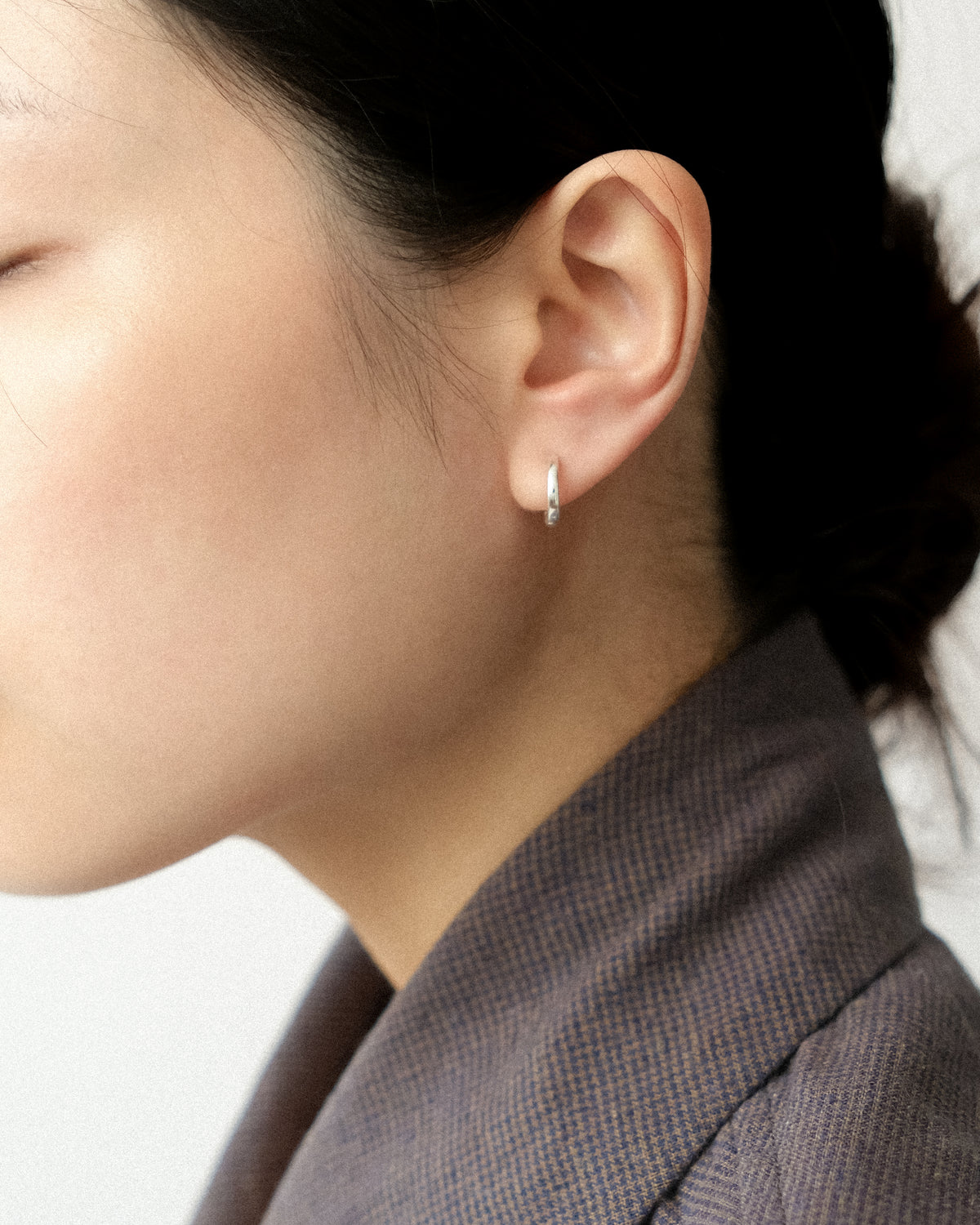 Close-up of an ear wearing a small hoop earring with a blurred background