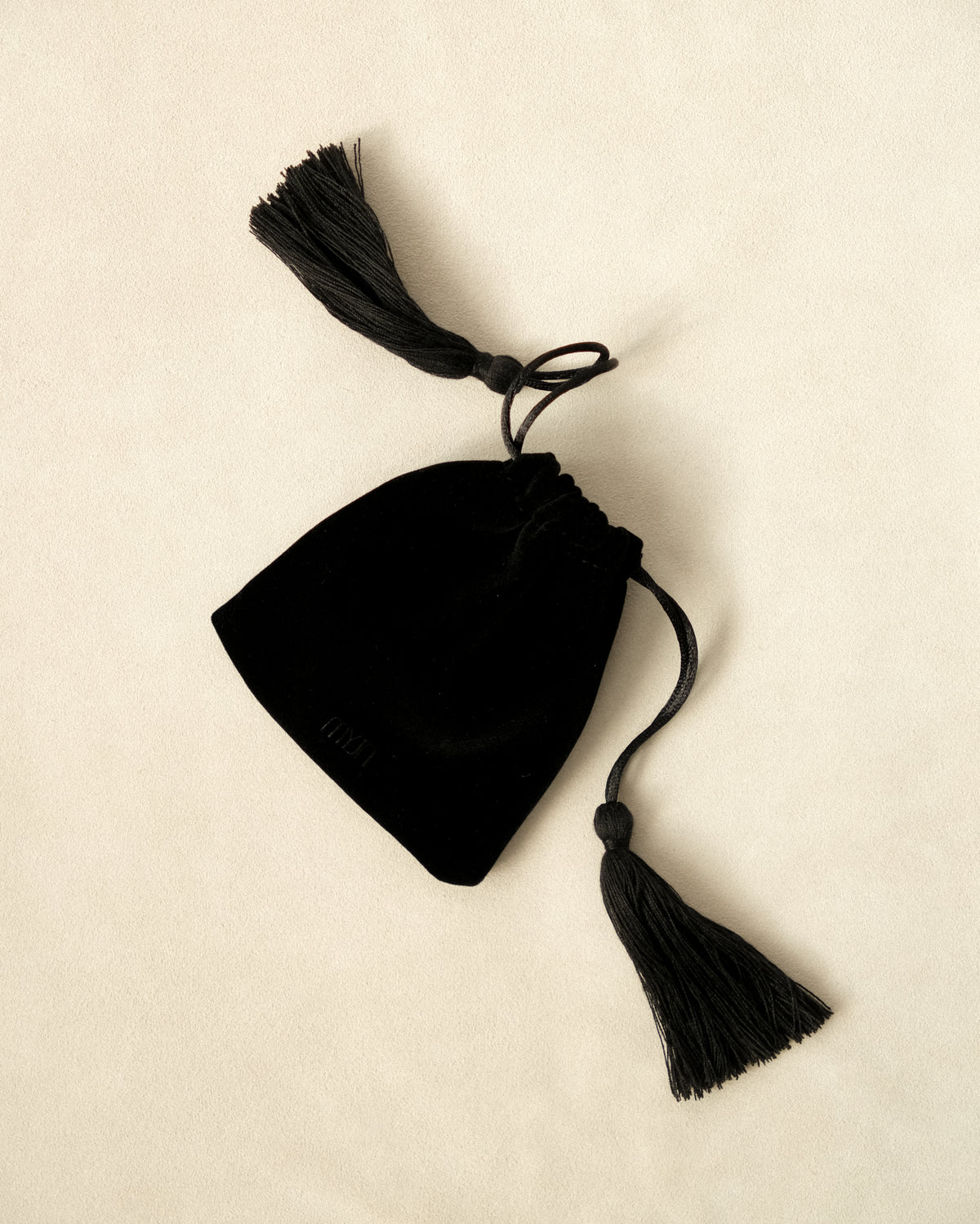 Black drawstring pouch with tassels on a beige background