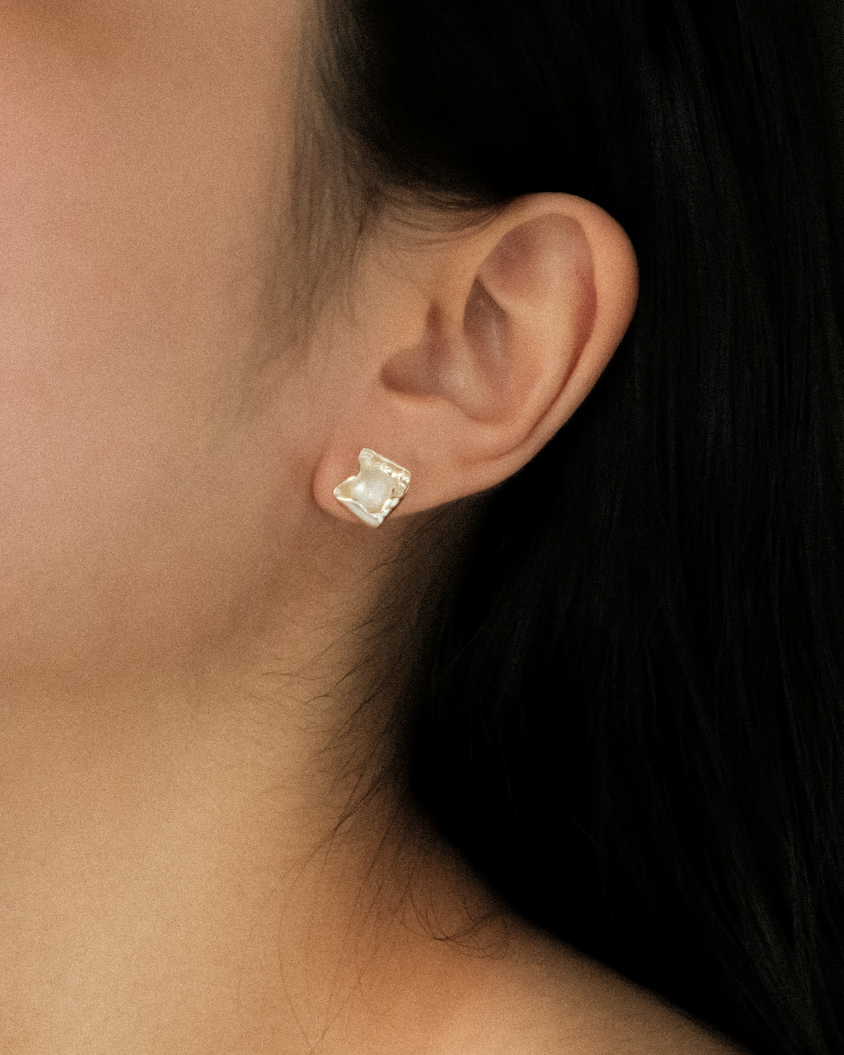 A close-up of a model’s ear wearing a small silver stud earring with a petal-shaped design featuring a central white freshwater pearl.