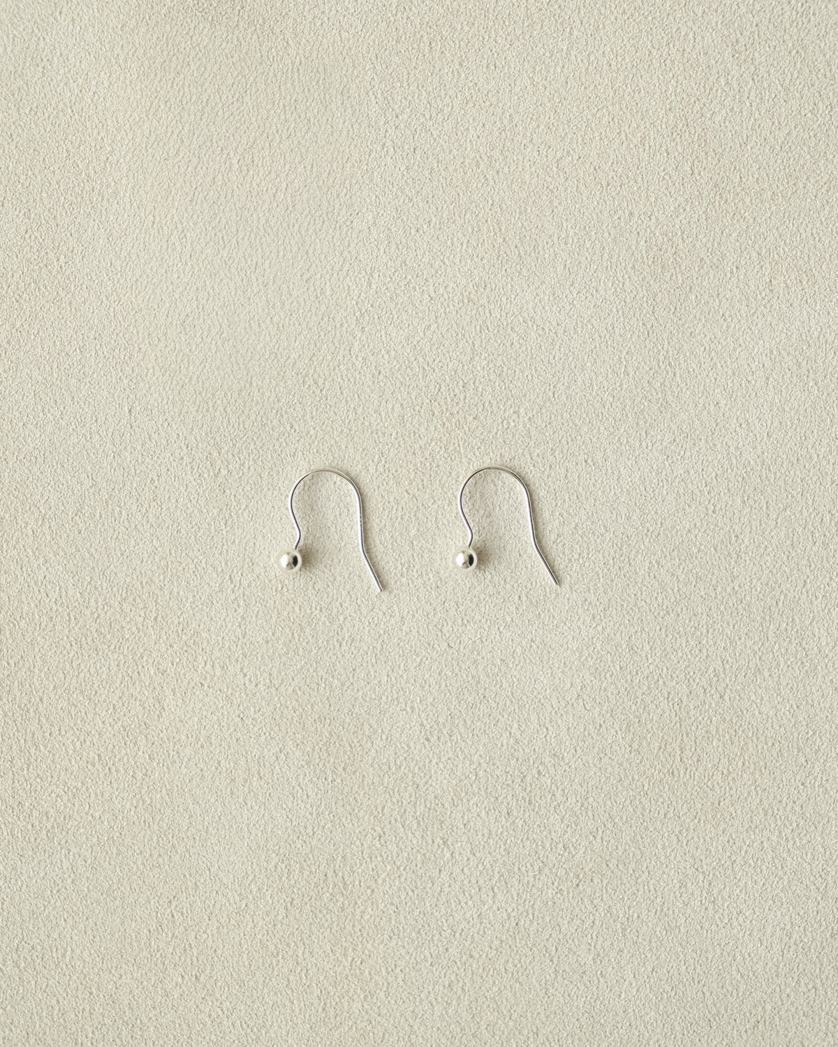 Pair of tiny silver dangle ball earrings on a beige background