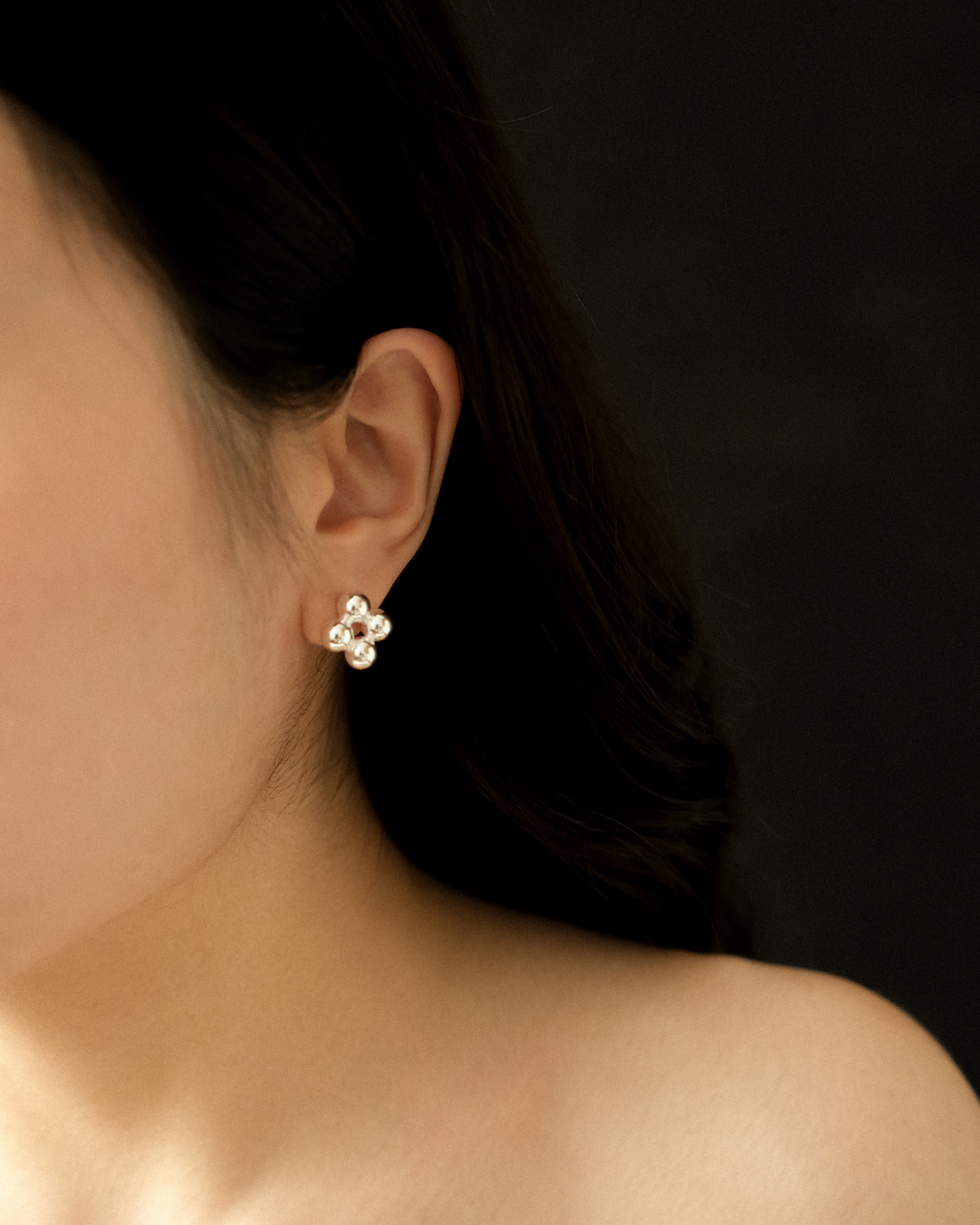 Close-up of an ear wearing a flower-shaped silver beaded earrings, captured from front with a black background