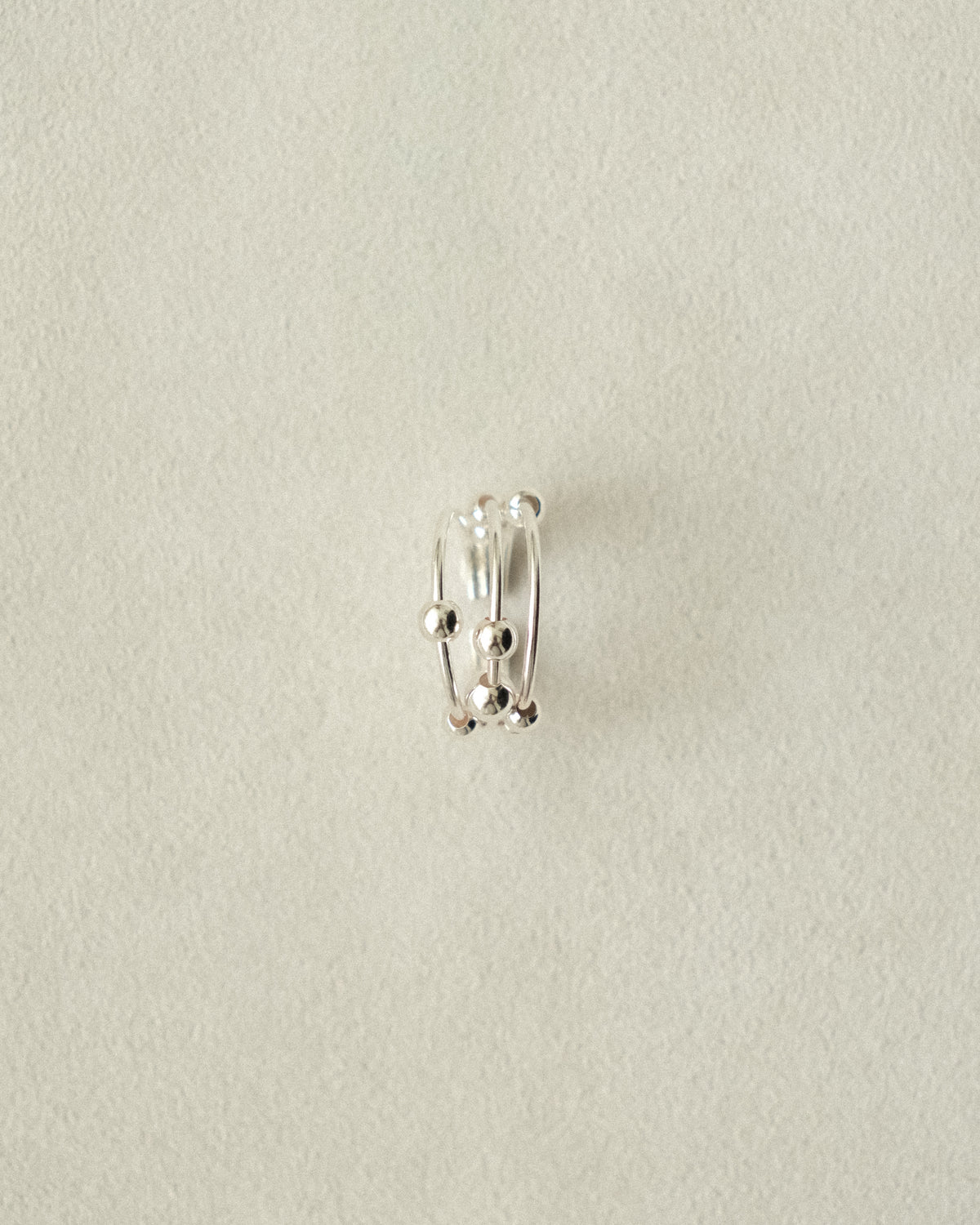 Trio silver ring accented with silver balls on a beige background