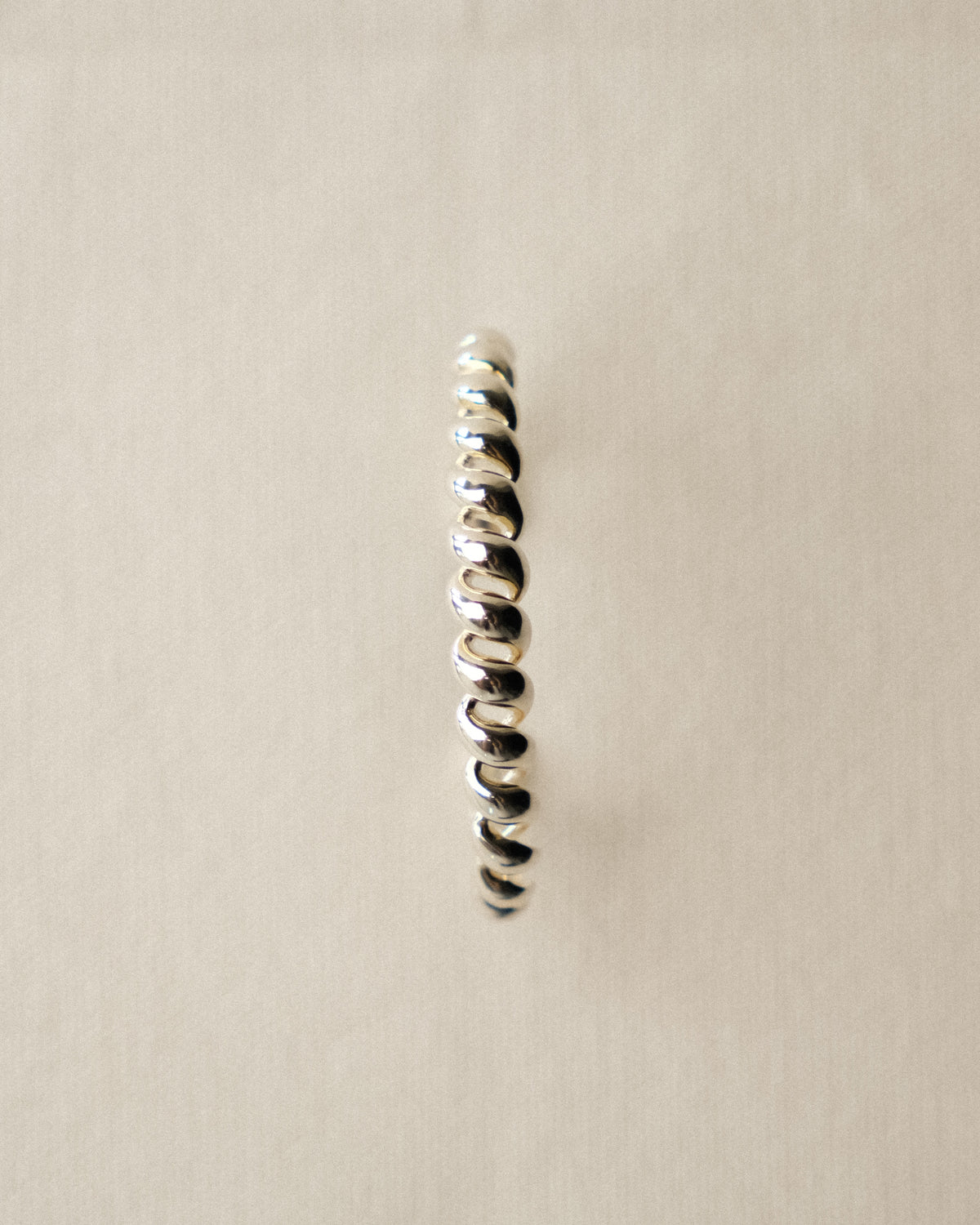 A single silver spiral cuff bracelet, reminiscent of a spiral staircase, displayed vertically against a plain, warm toned tablecloth background.