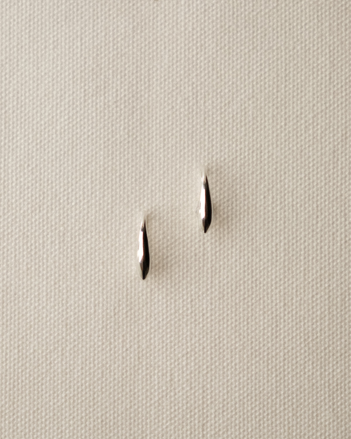 A pair of silver orzo pasta-like, shot against a cream-white fabric background.