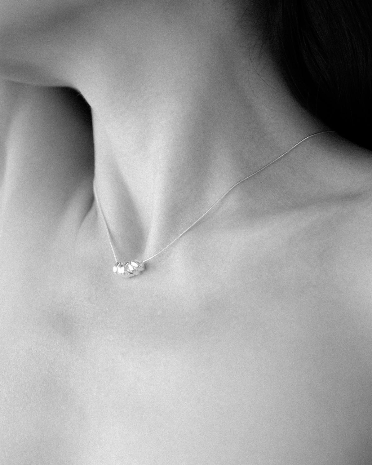 A close-up black and white photograph of a model's neck wearing a delicate silver necklace with a small cluster of polished silver round pendants at the center.