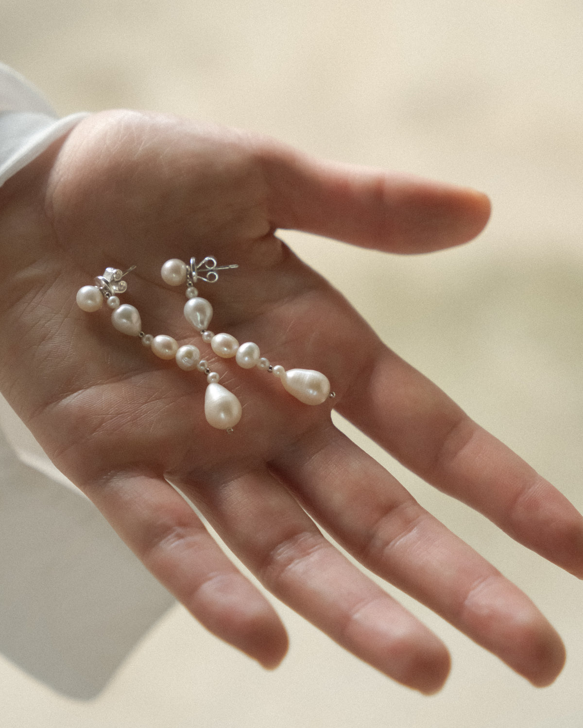 Long pearl earrings held in a hand against a neutral background