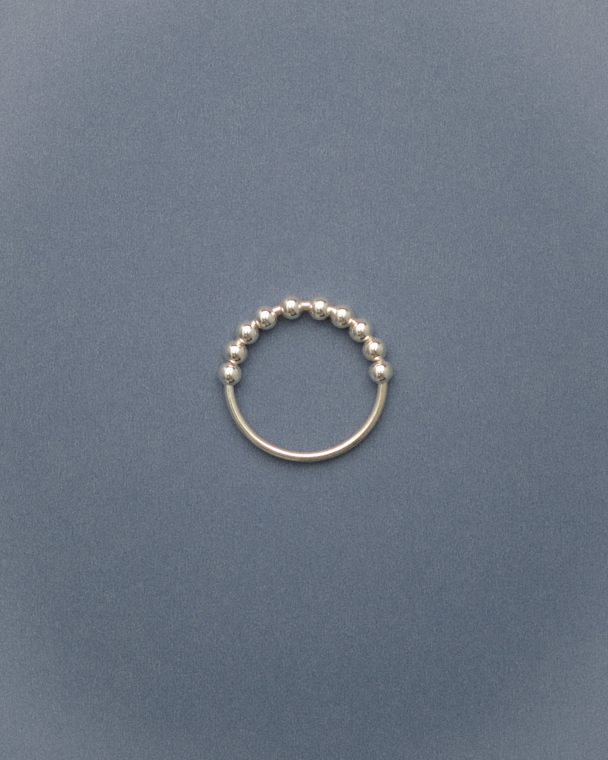 Silver flowing bead ring on a grey-blue background