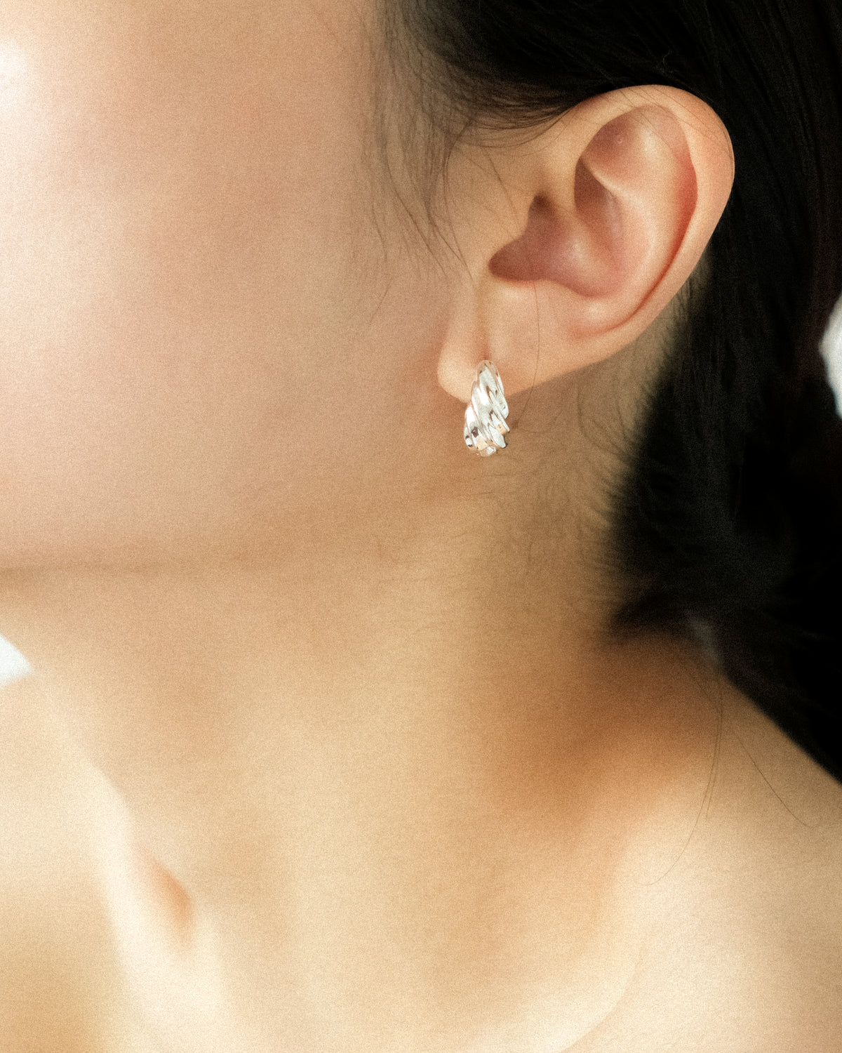 Close-up of an ear wearing a silver-plated brass spiral earring with a blurred background