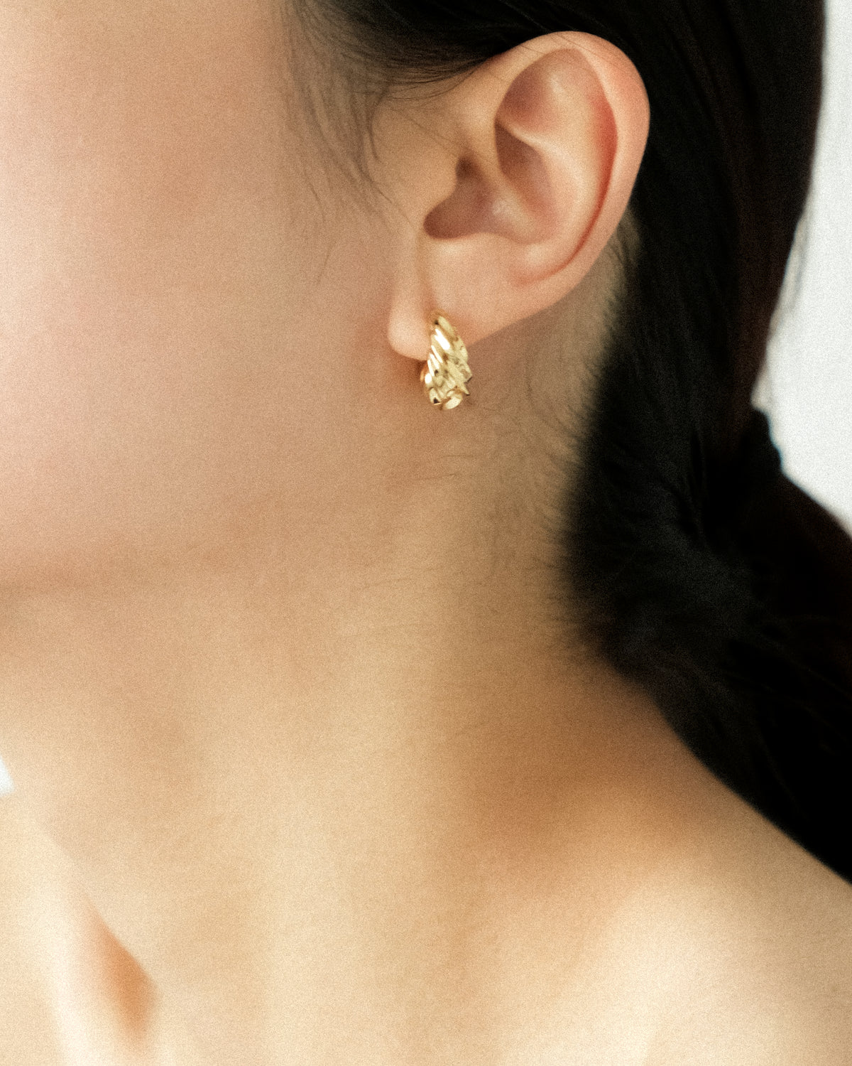 Close-up of an ear wearing a gold-plated brass spiral earring with a blurred background