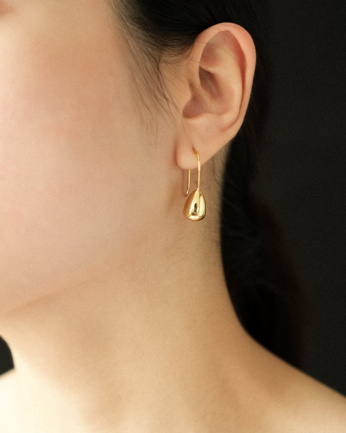 Gold teardrop earring worn by a person against a dark background
