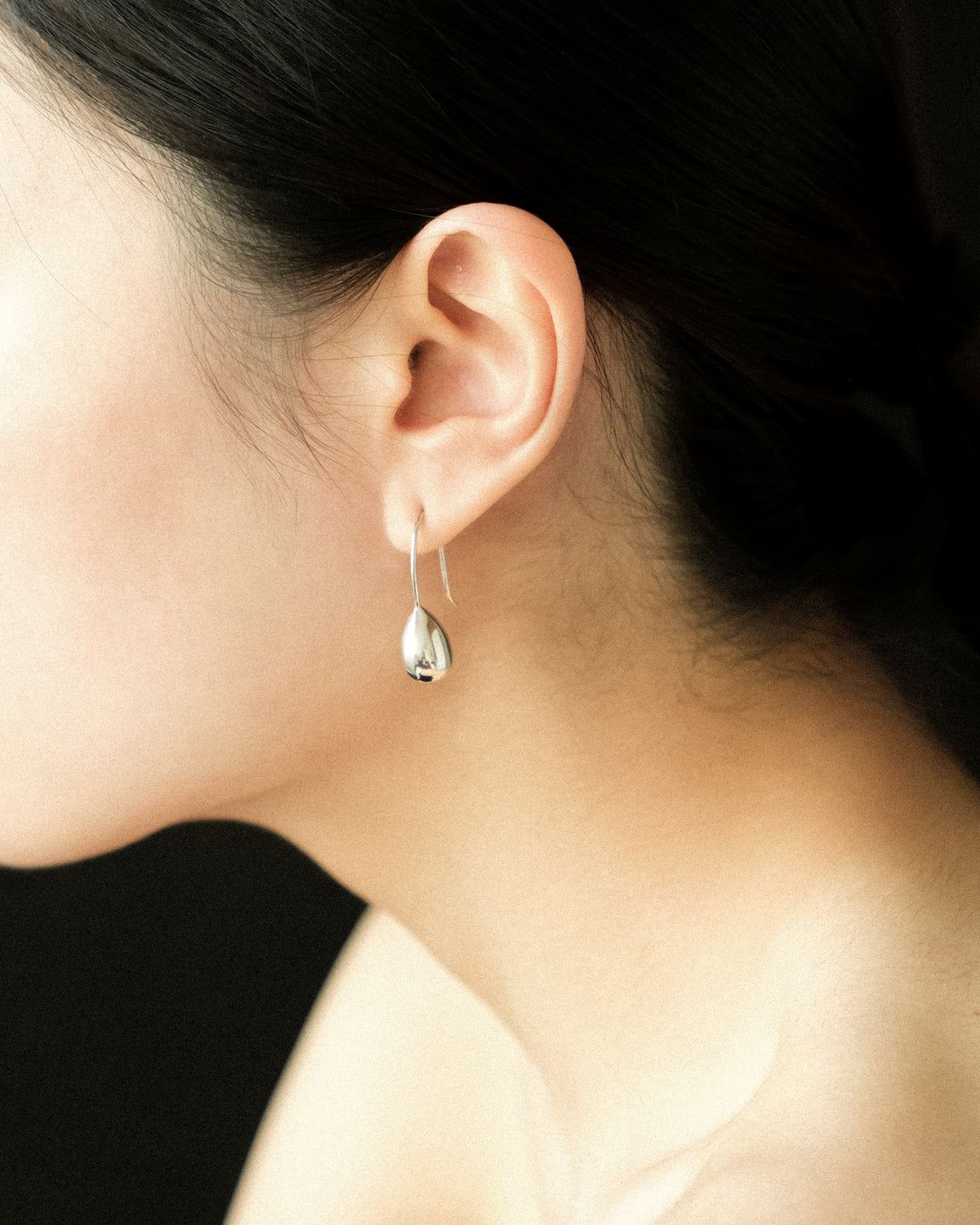 Close-up of a person wearing a silver teardrop earring with a black background