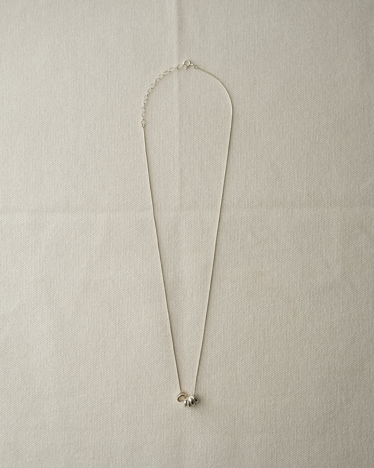 A delicate silver necklace with 3 round silver pendants, displayed on a textured beige fabric background.