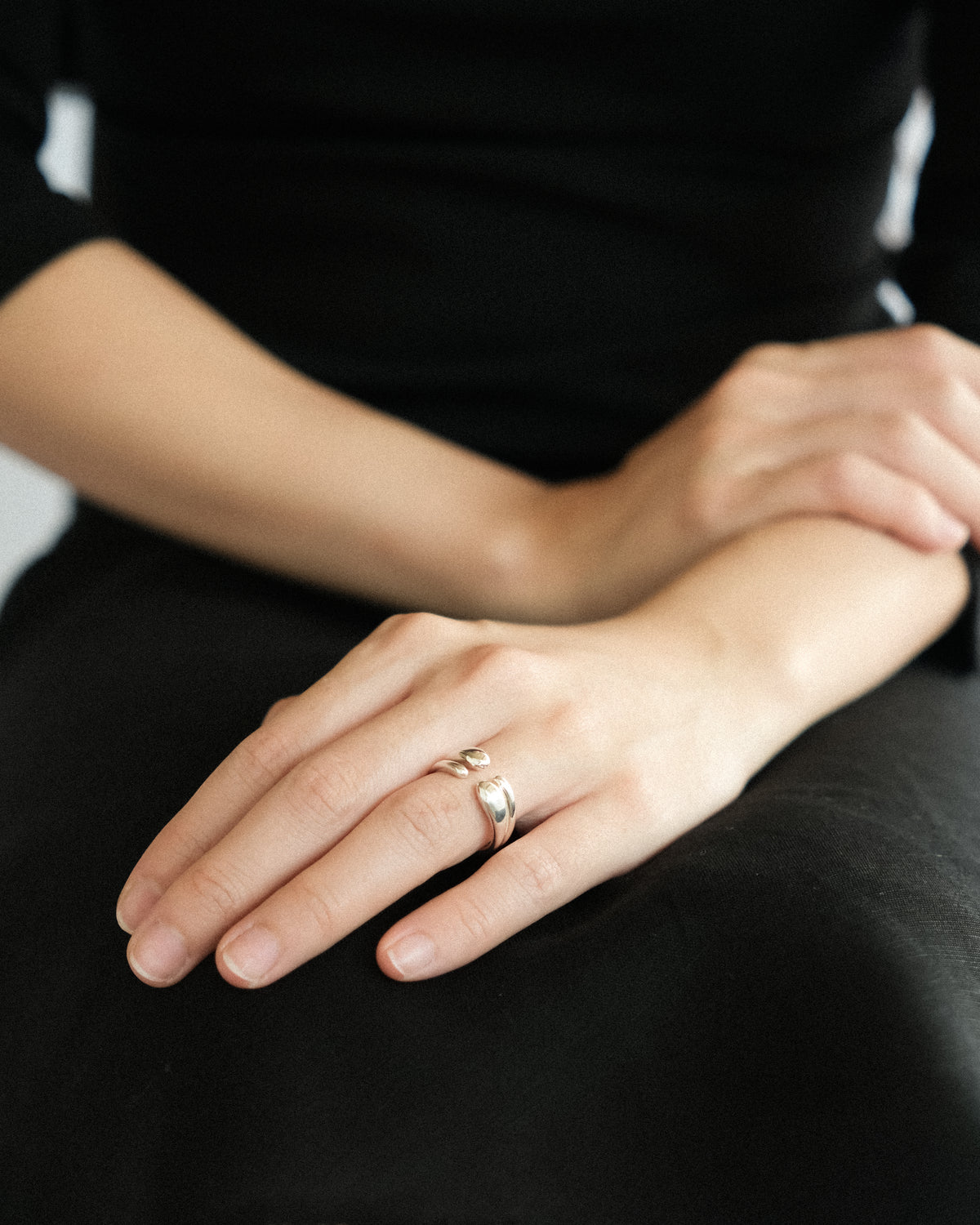 Close-up of a hand wearing a silver double droplet ring on a white background