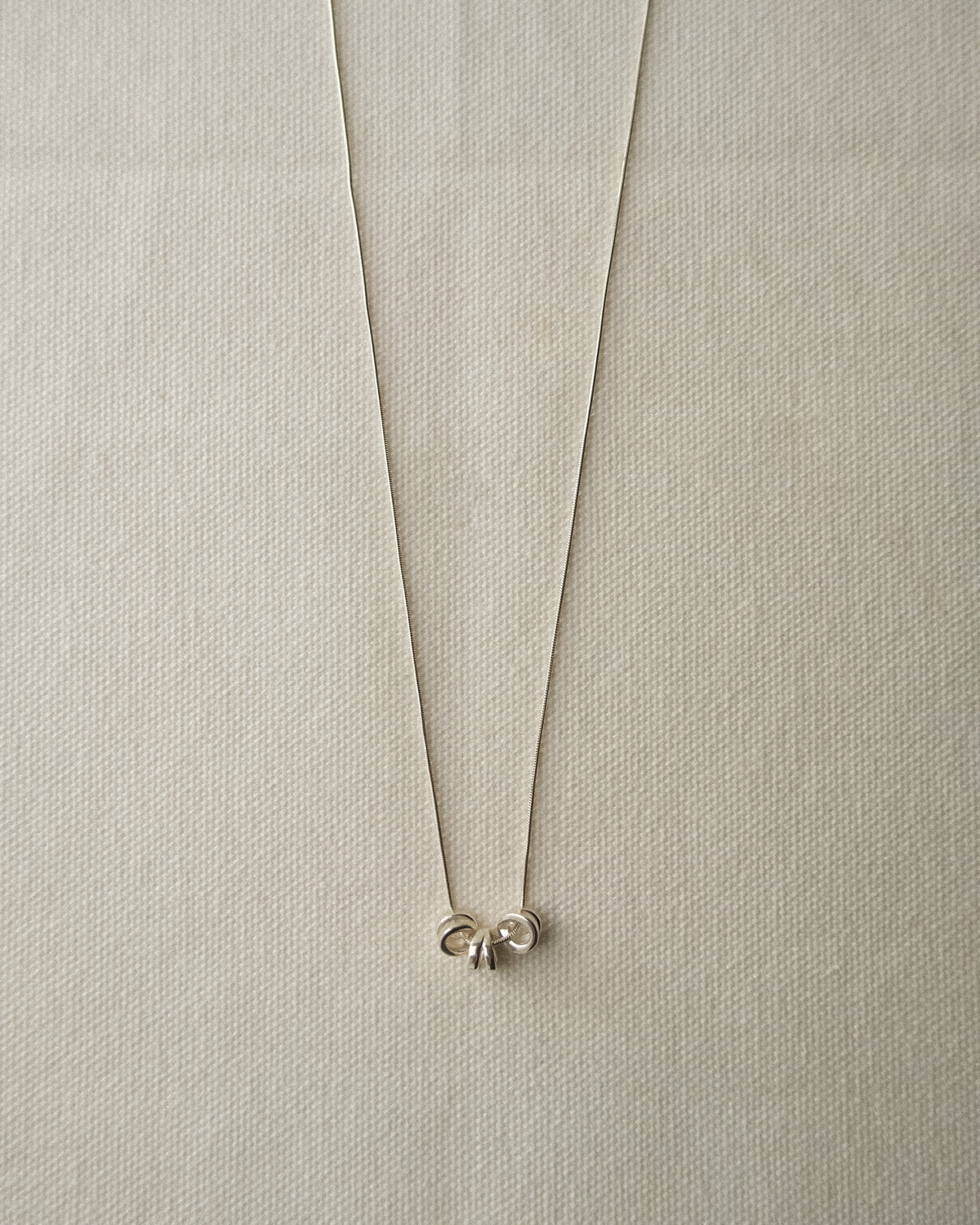 A delicate silver necklace with 3 round silver pendants, displayed on a textured beige fabric background.