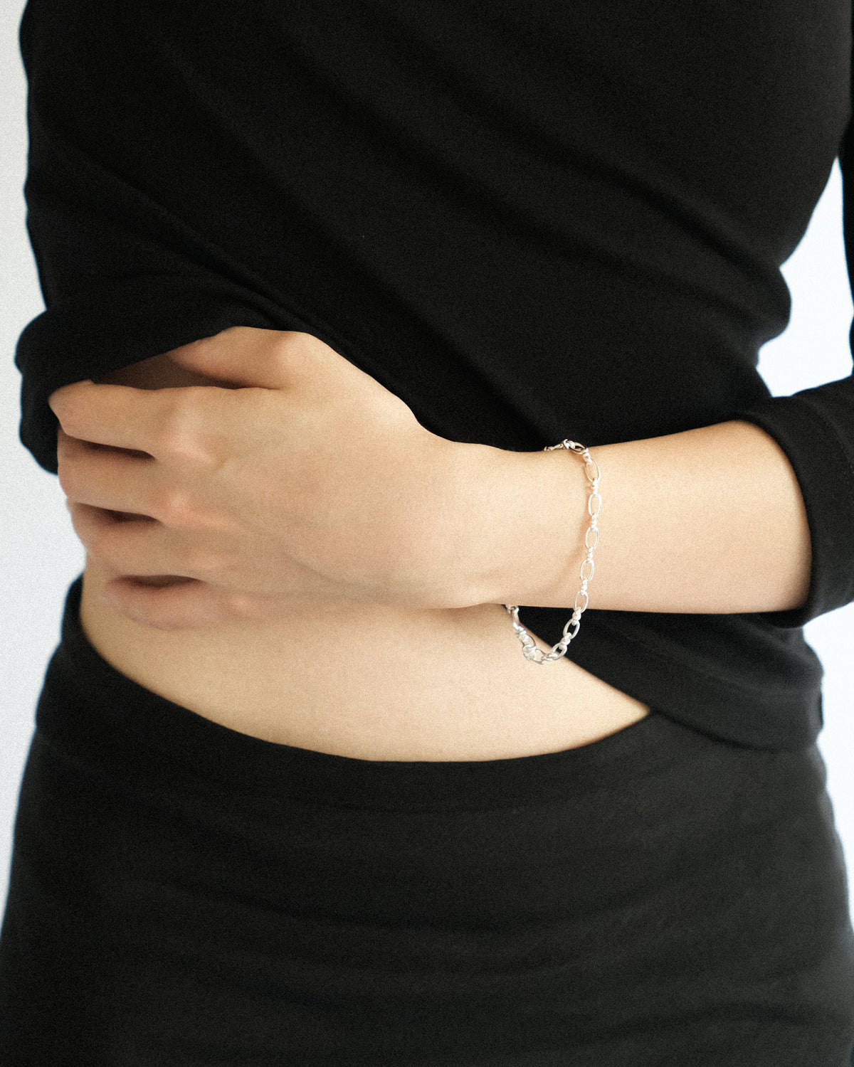Person wearing a delicate silver chain bracelet against a plain background