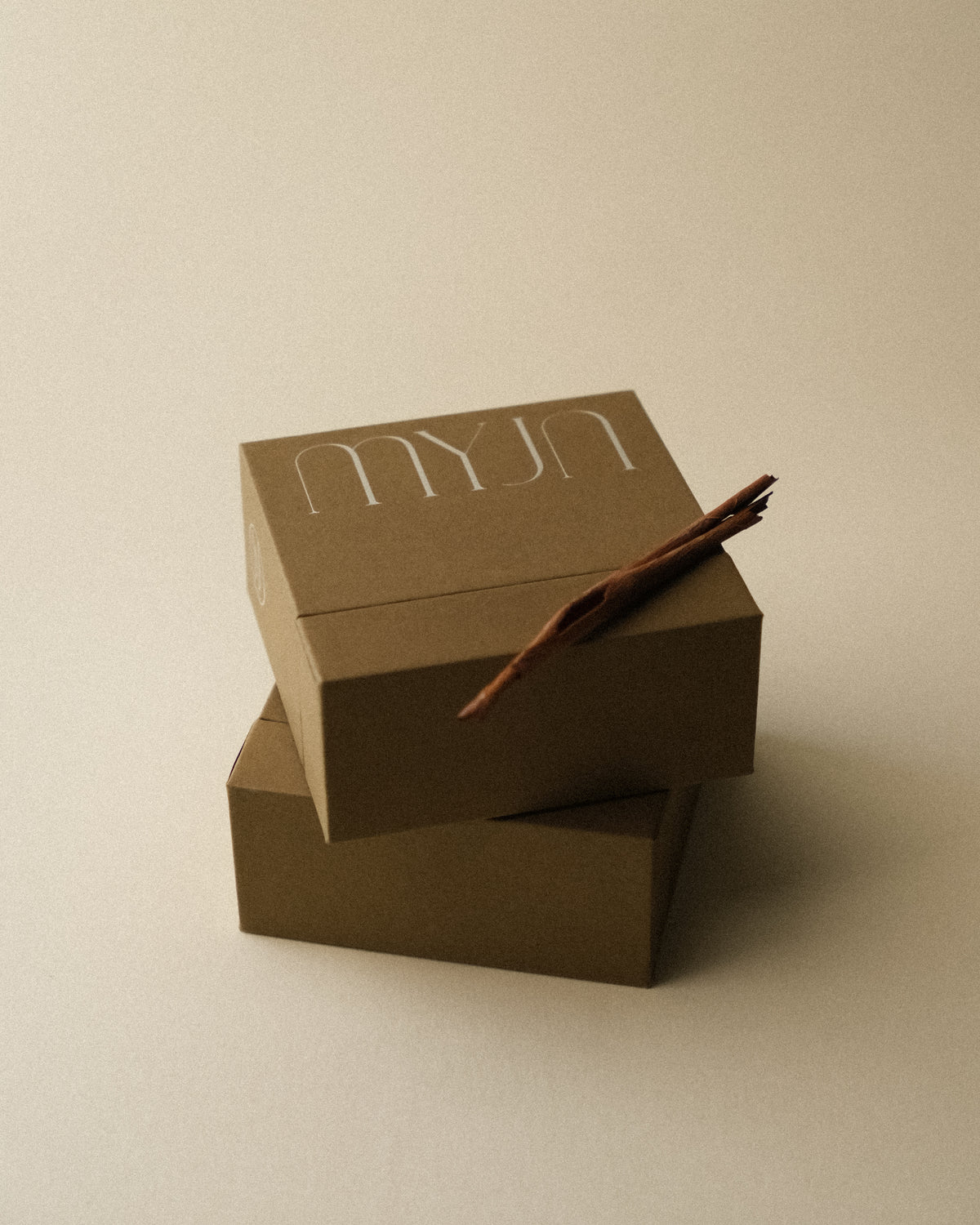 Two light khaki brown jewellery boxes stacked together with a piece of tree bark as a prop, photographed on a warm toned wabi sabi backdrop. The earthy hue echoes the natural colour of the bark.