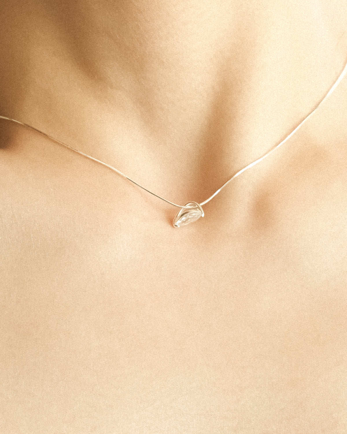 A close-up of a woman wearing a marquise diamond pendant necklace, revealing the side profile of its vase-inspired silhouette.