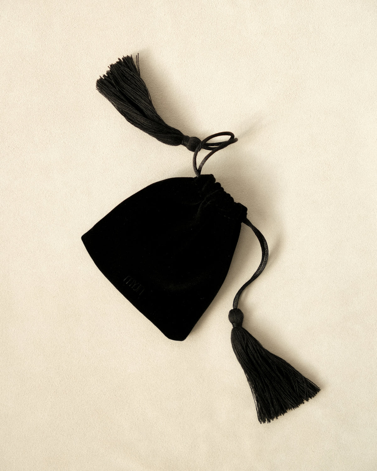 Black drawstring pouch with tassels on a beige background