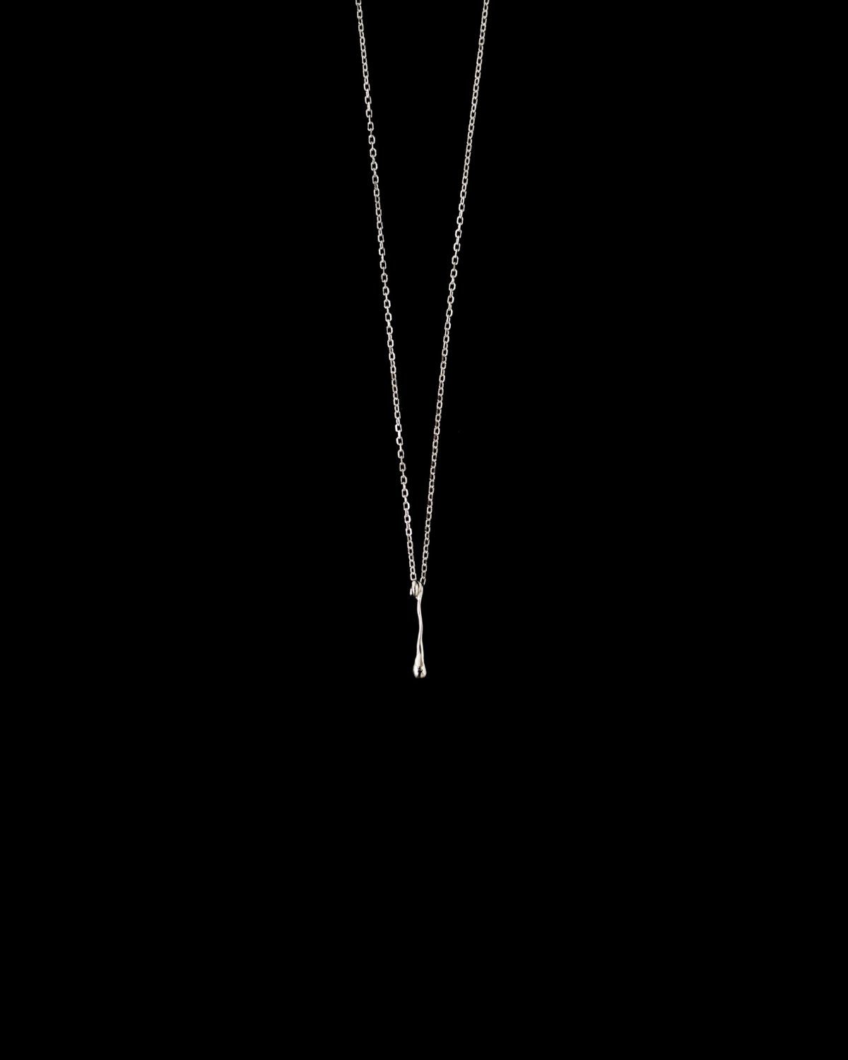 Close-up of a necklace featuring the silver fluid drop pendant on a black background.