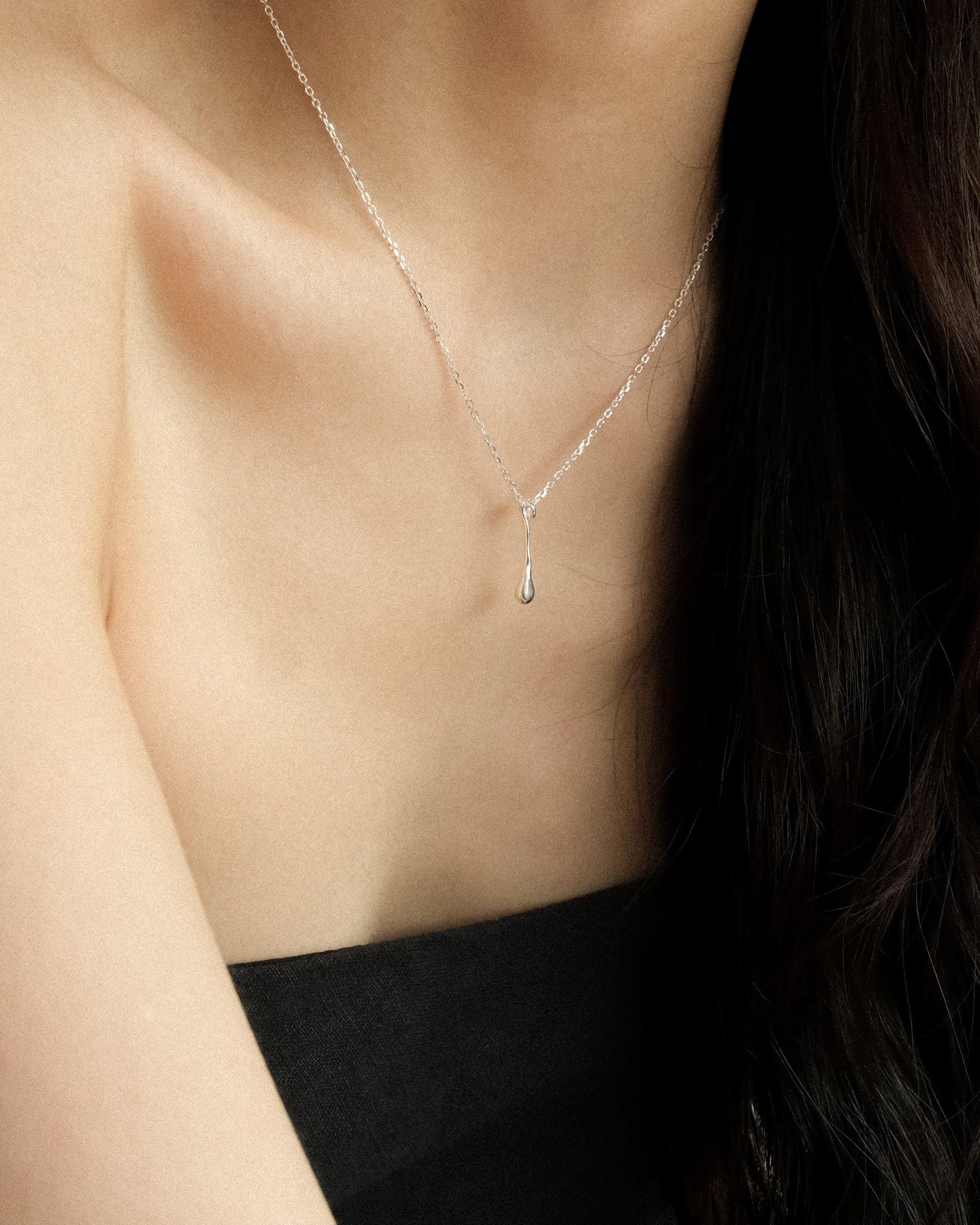 Silver chain necklace with a silver fluid drop pendant on a person wearing a black tube top.