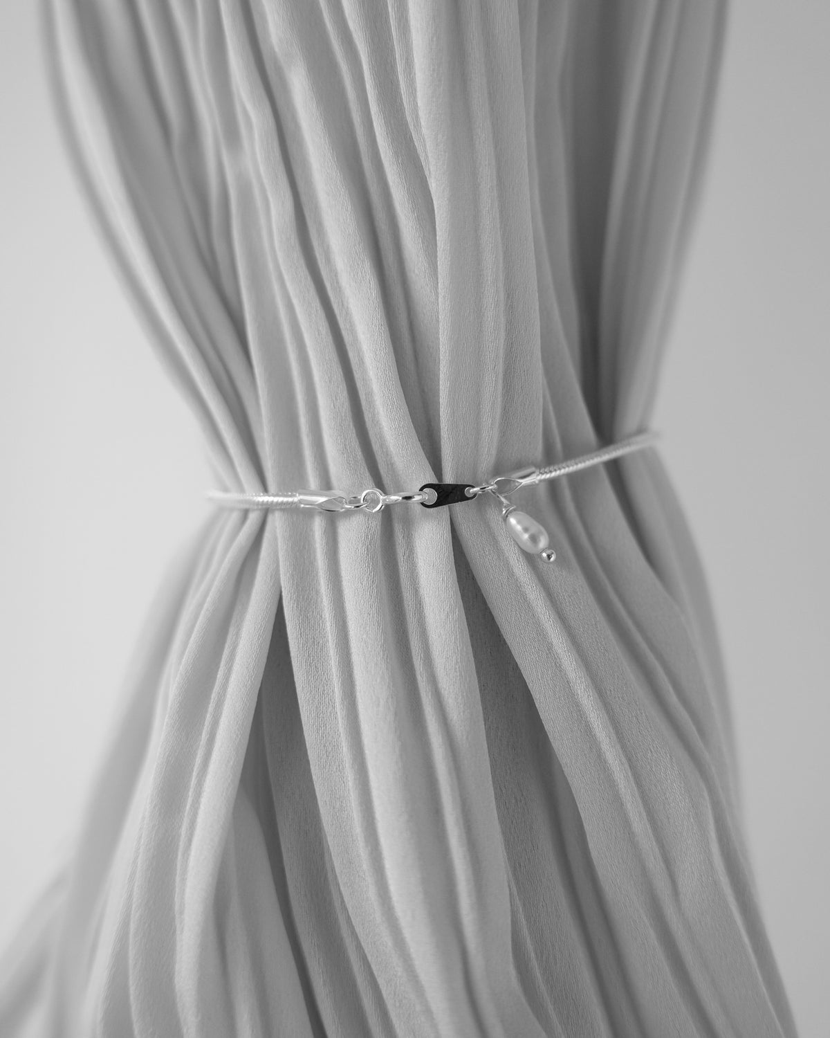 Close-up of a gray curtain with a tieback against a neutral background
