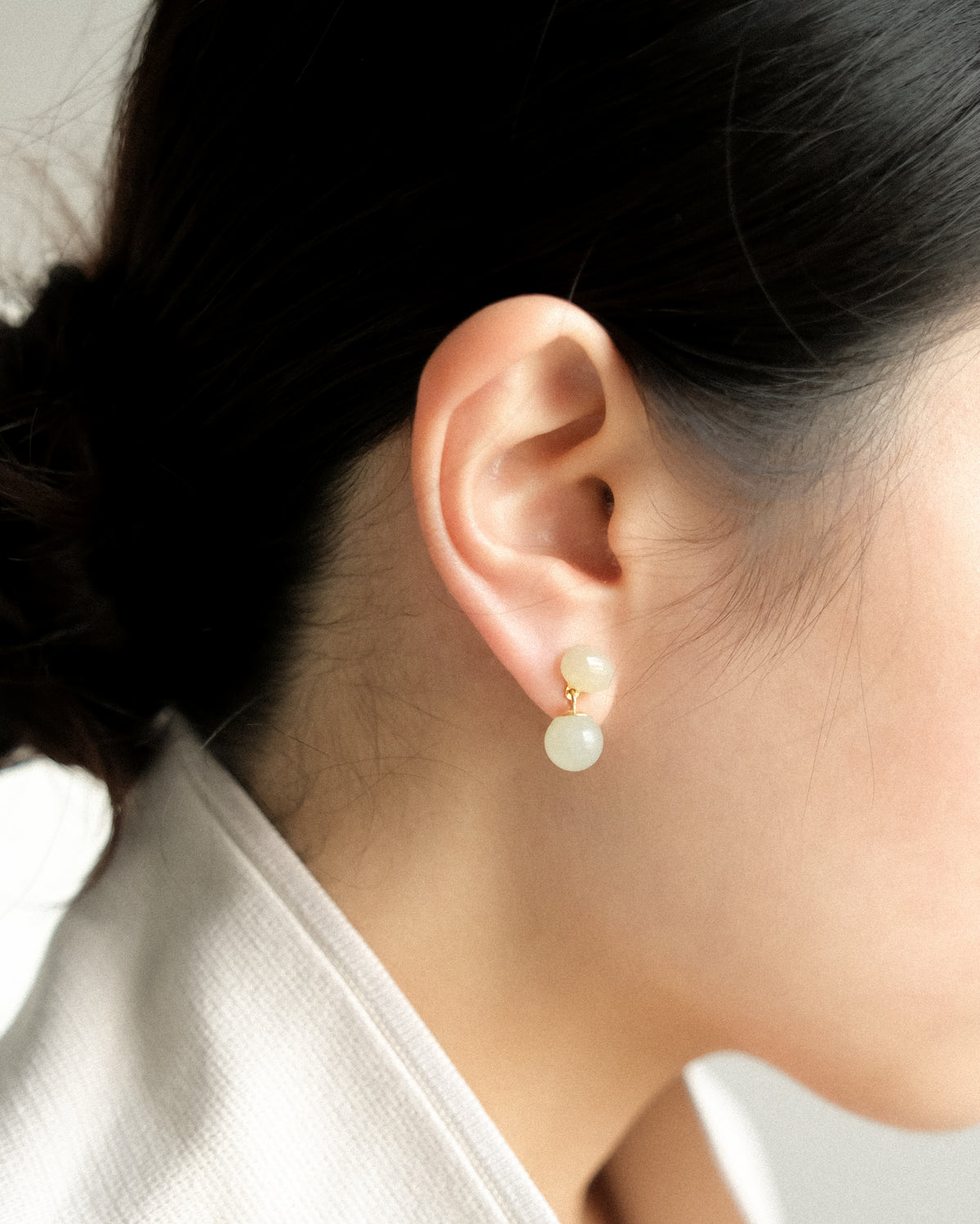 Close-up of an ear wearing a Hetian Jade drop earring with a white background