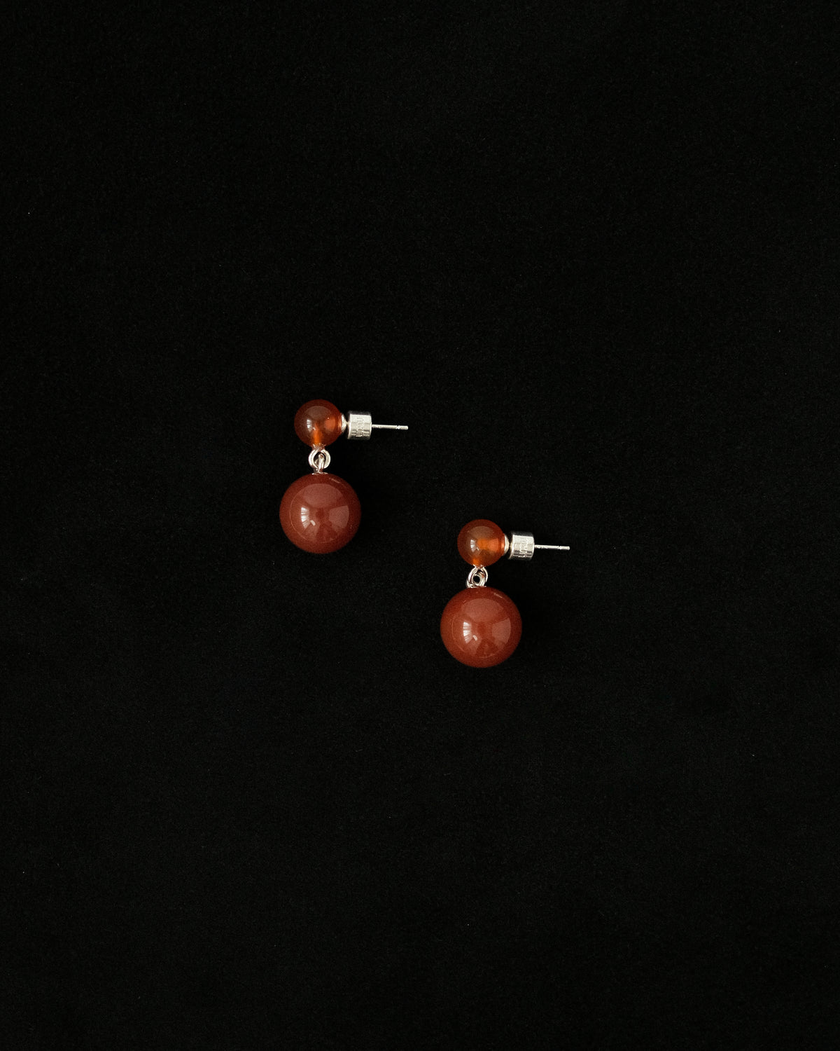 Pair of earrings with red spherical stones on a black background