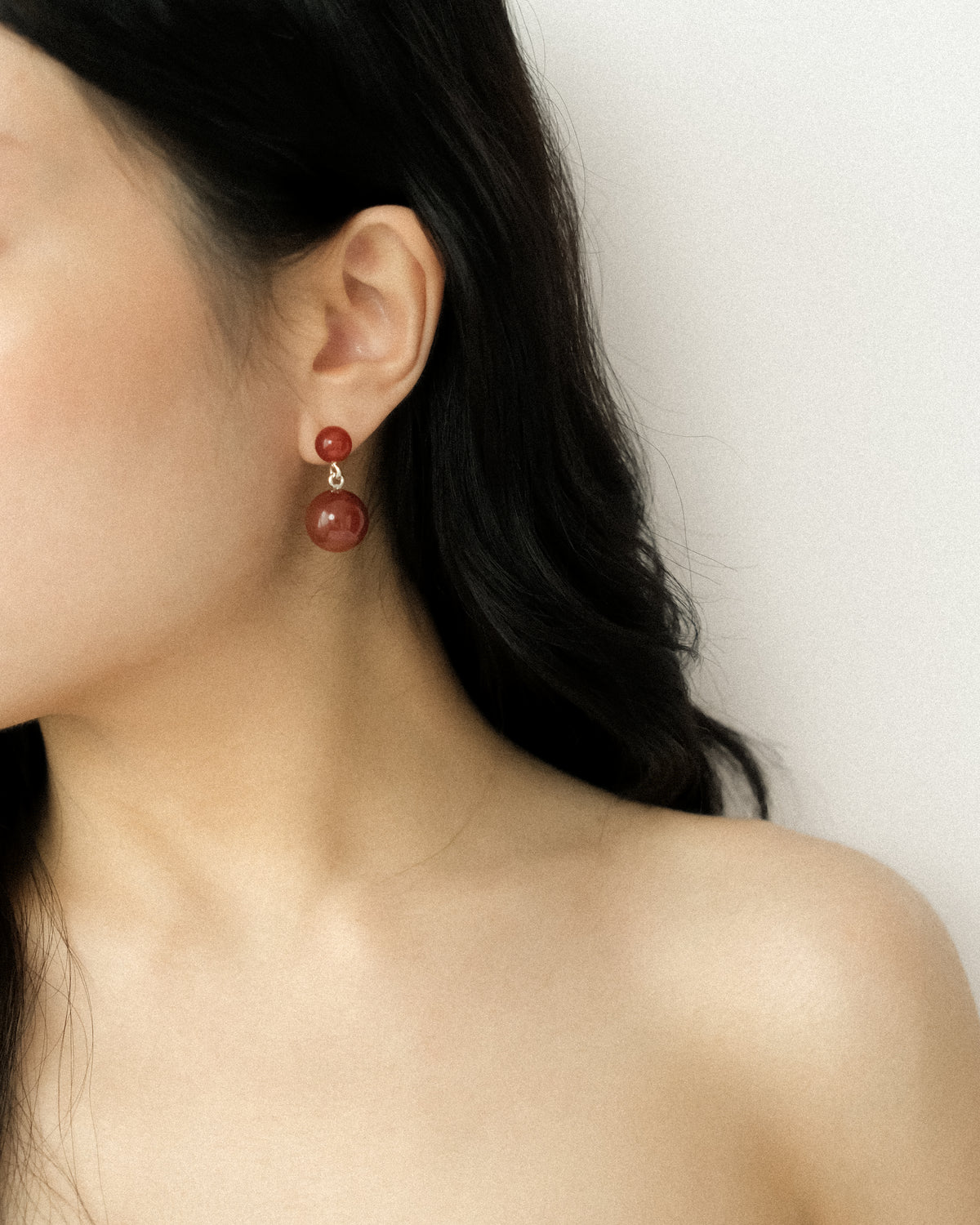Close-up of a person wearing red earrings with a neutral background
