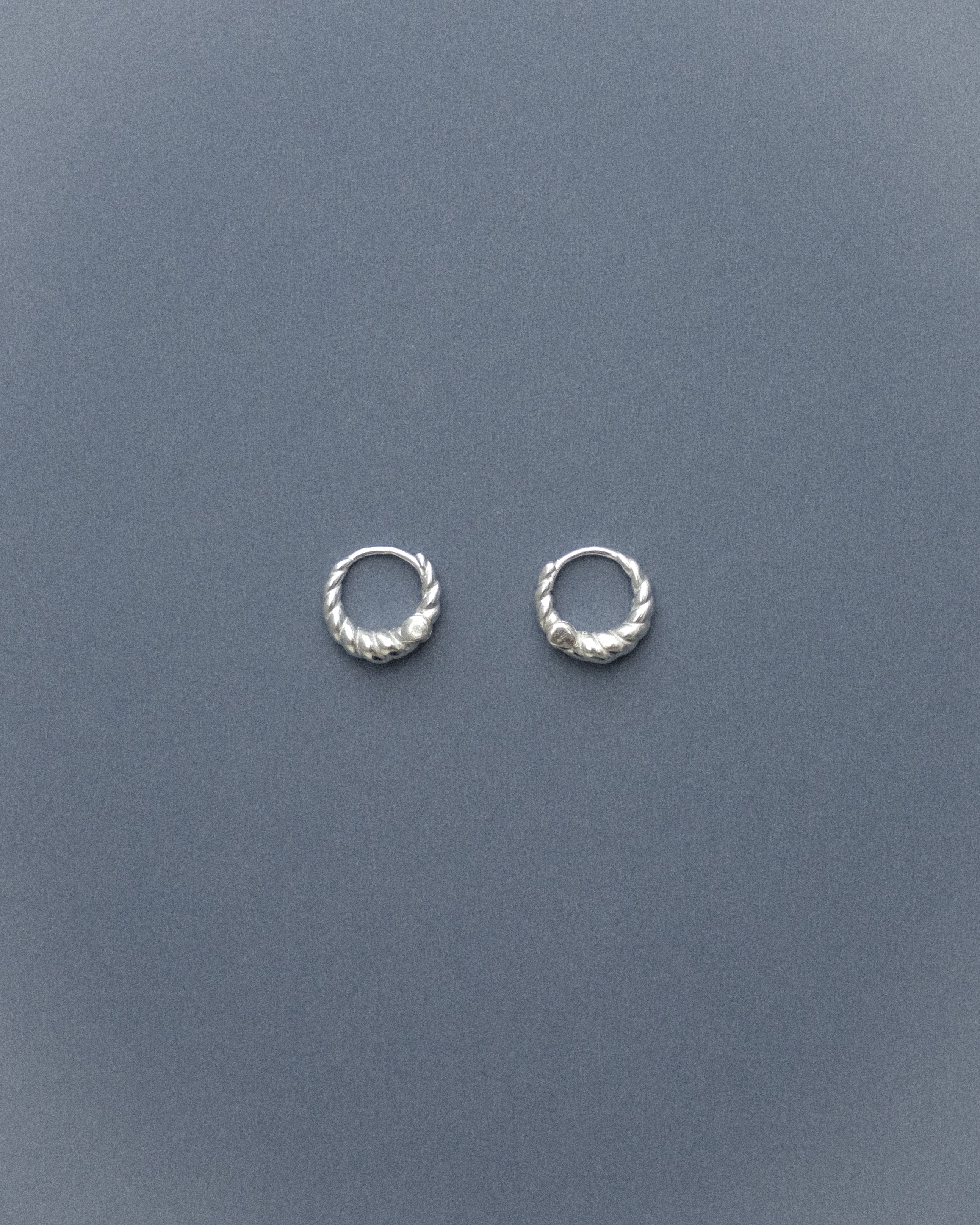 Silver sipral hoop earrings on a grey-blue background