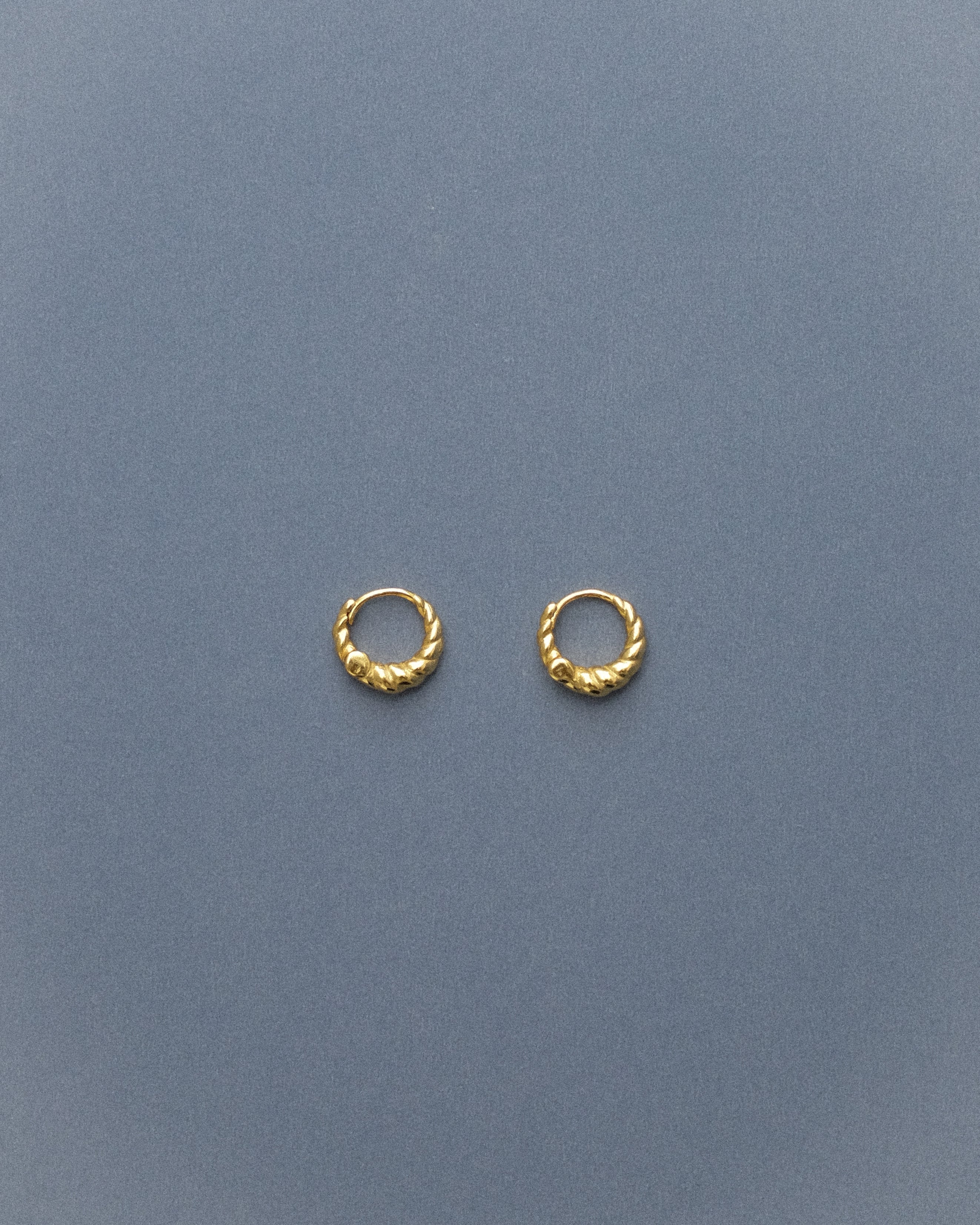 Gold sipral hoop earrings on a grey-blue background