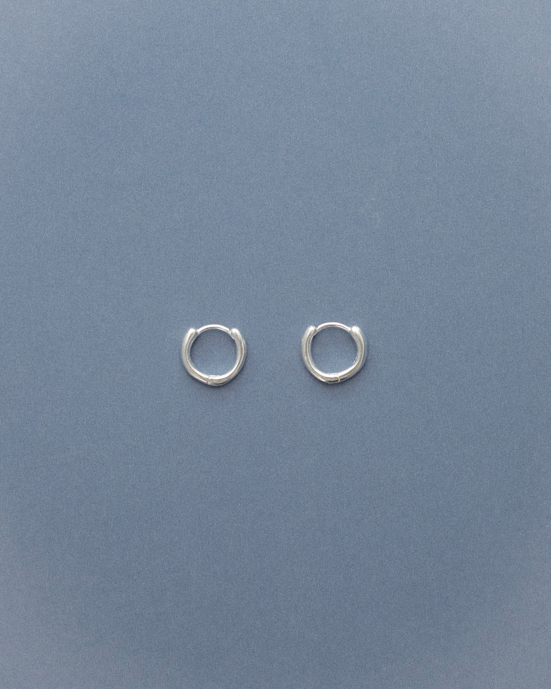 Small silver sulptural hoop earrings on a grey blue background