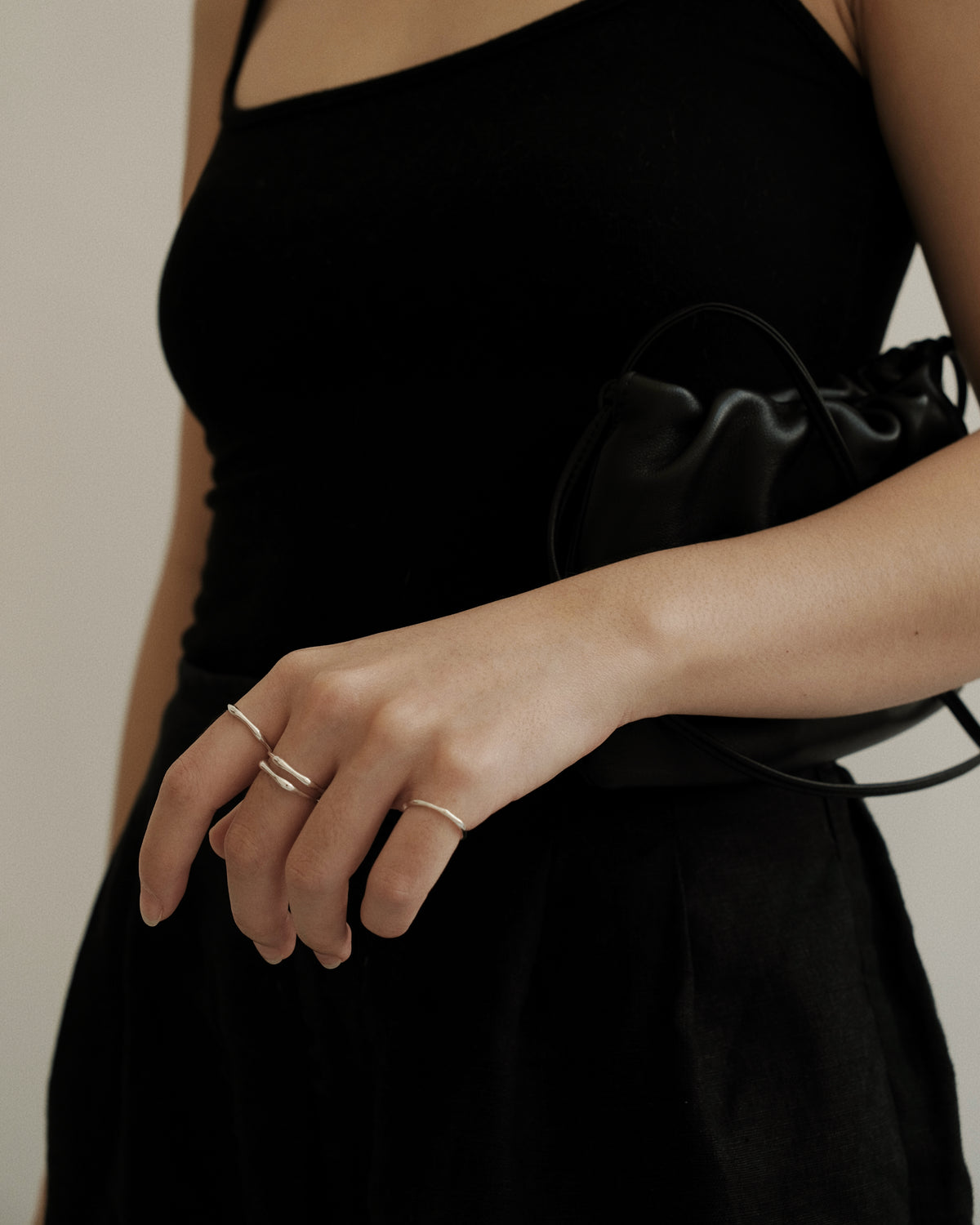 A person wearing a black dress is showcasing silver thin band rings on their fingers. The rings appear delicate and are worn on multiple fingers.